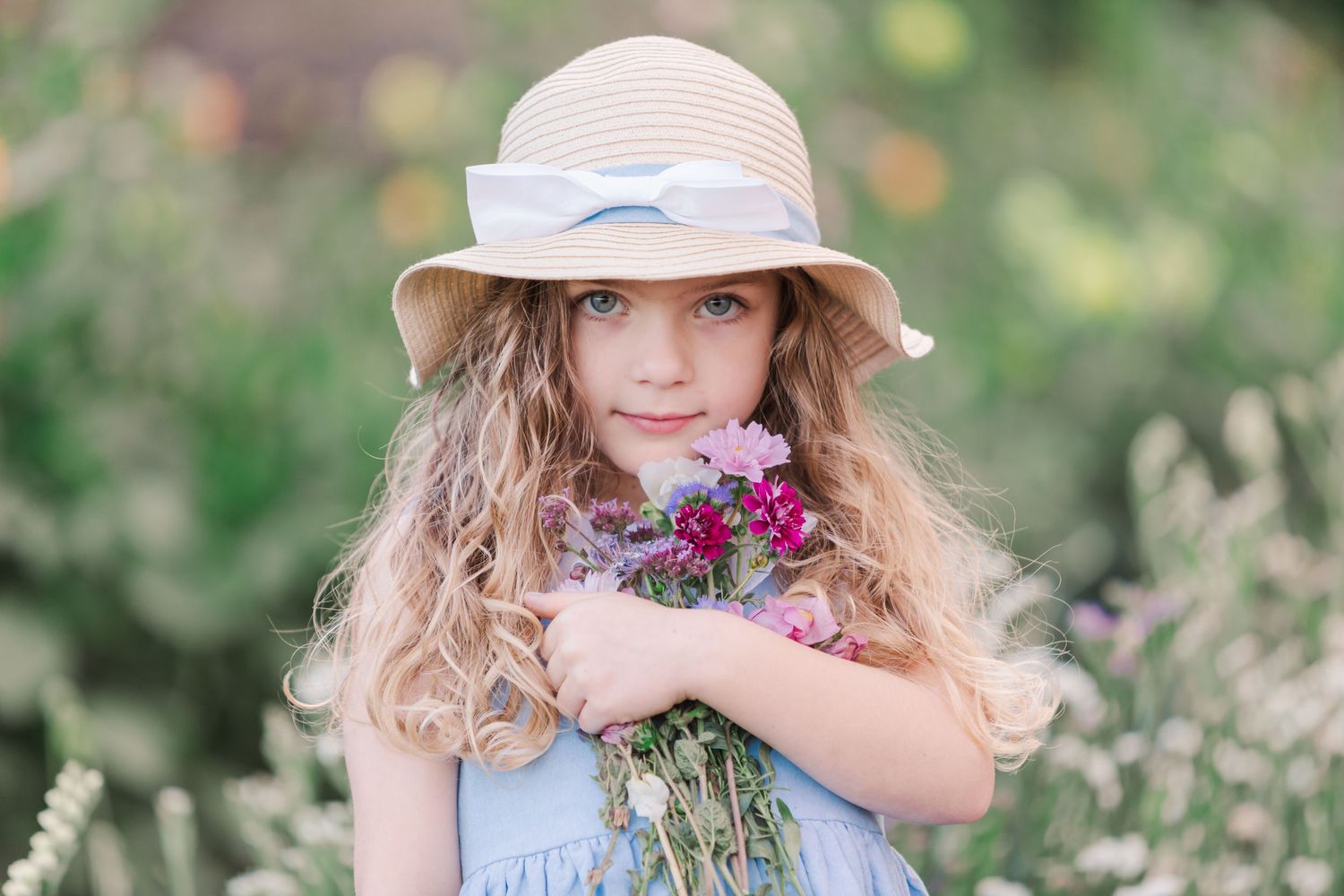 Young girl in sun hat holding purple wildflowers in summer garden.