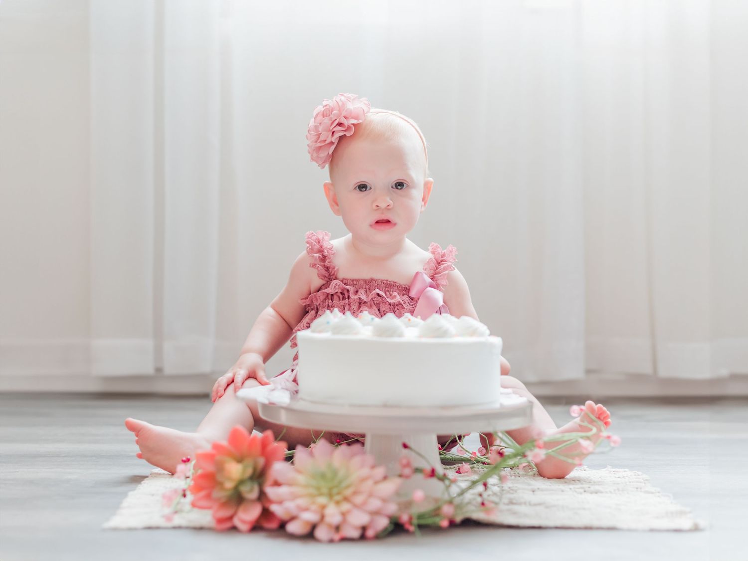 White cake smash photography setup with pink flowers and natural light.