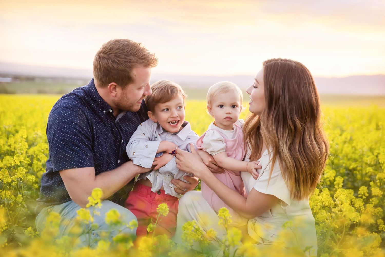 Family enjoying tender moments together in blooming yellow canola field at sunset.