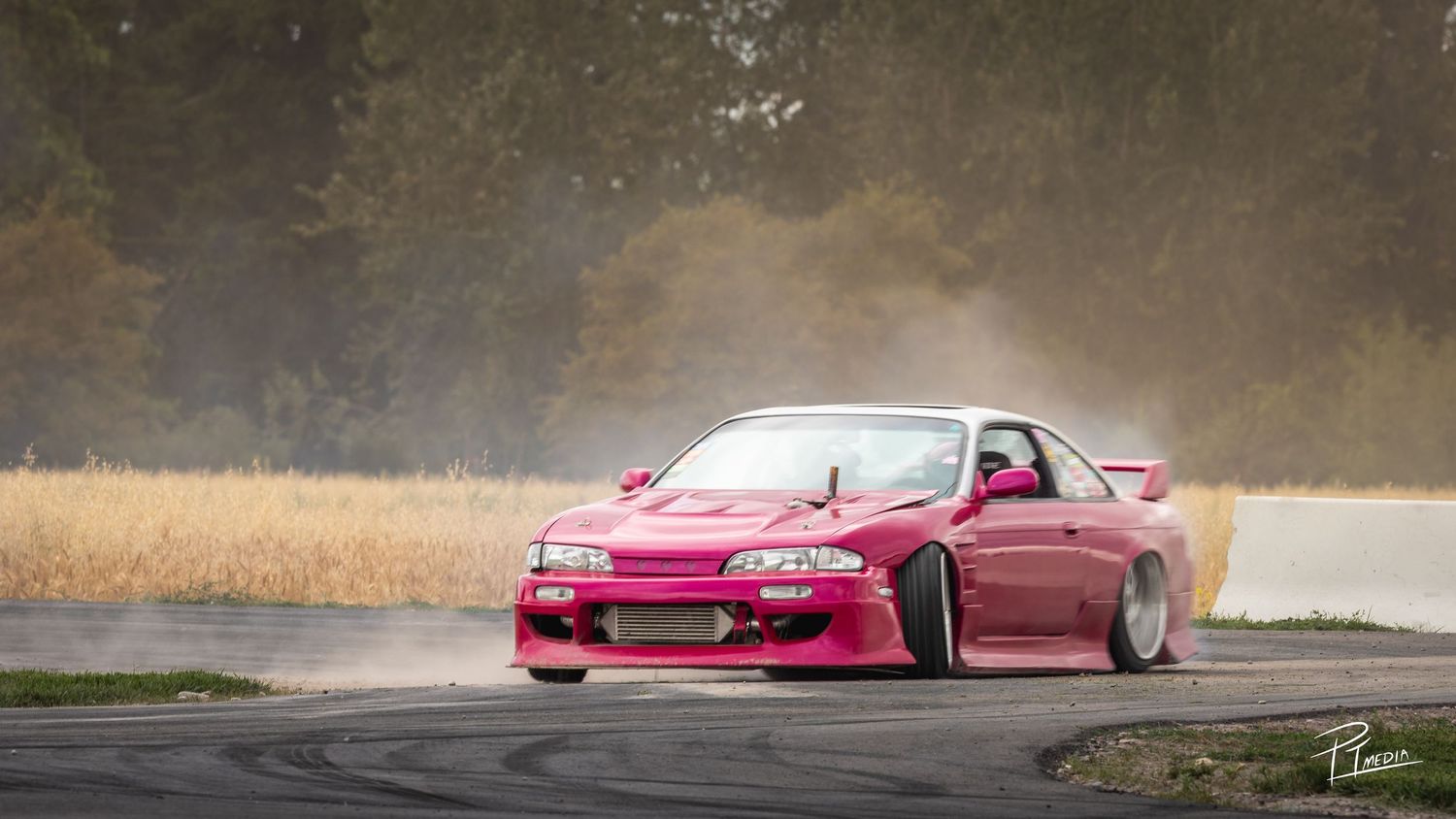 Pink drift car performs smoky burnout on race track during motorsport competition.