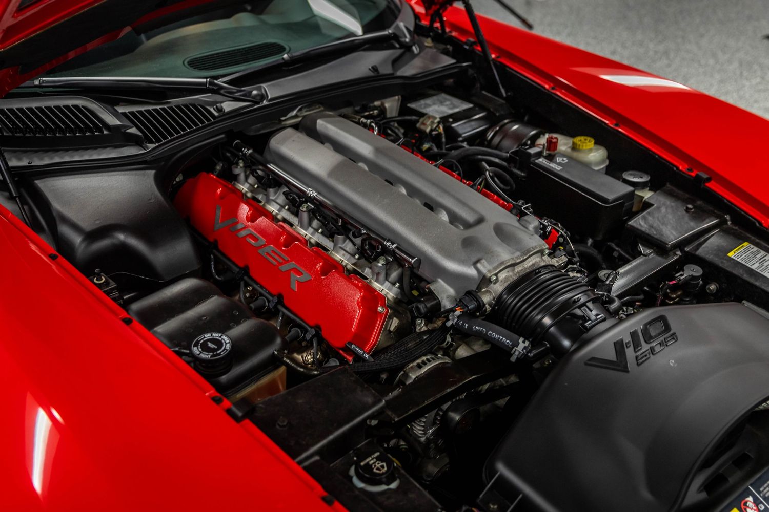 Close-up view of a bright red car hood open to reveal a detailed engine bay with chrome and metal components.