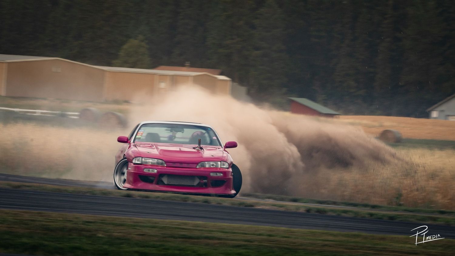 Pink drift car creates dramatic smoke trail while sliding sideways on racetrack during competition.