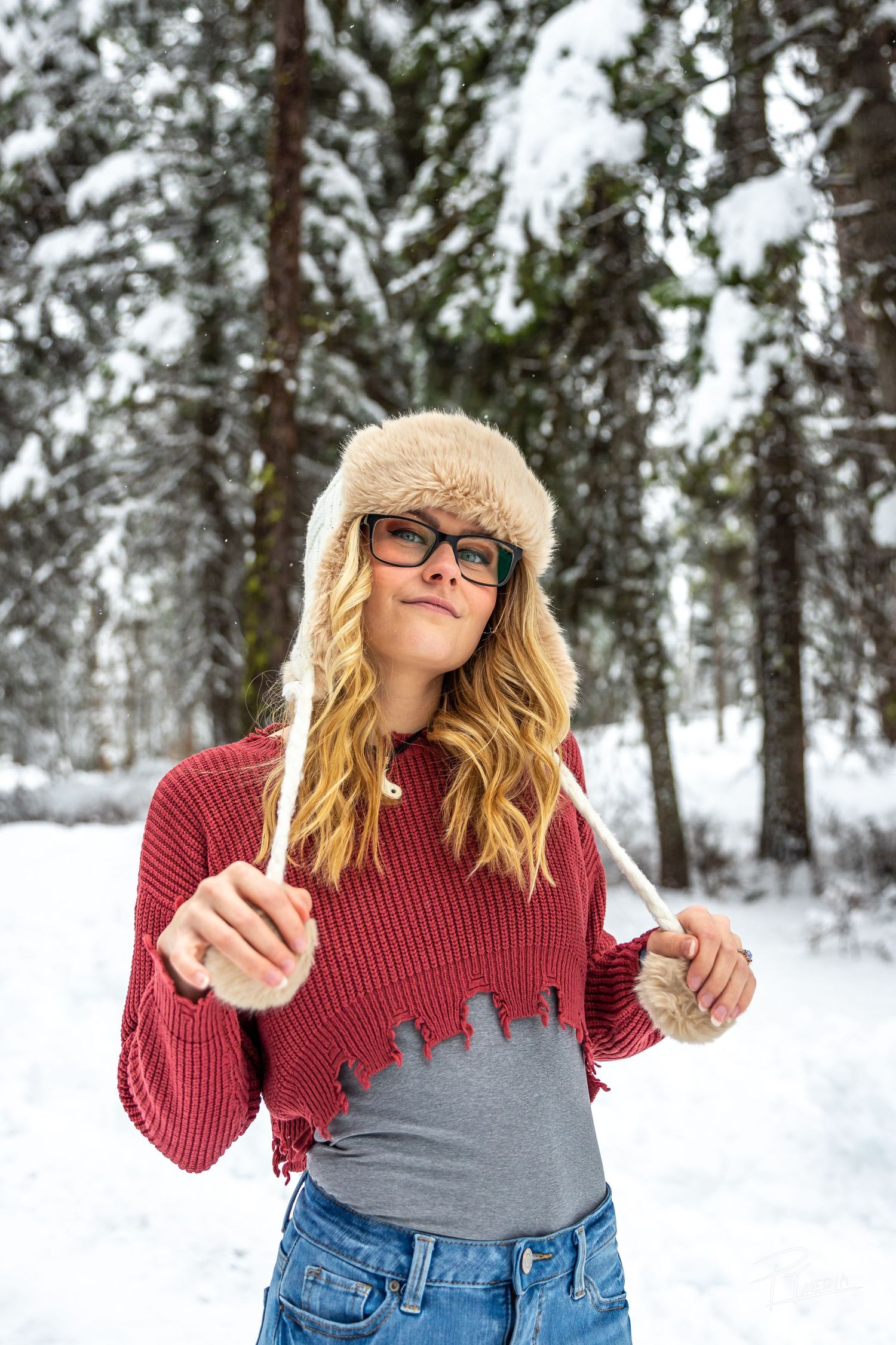 Person wearing red sweater and winter hat strikes playful poses against snowy forest backdrop.