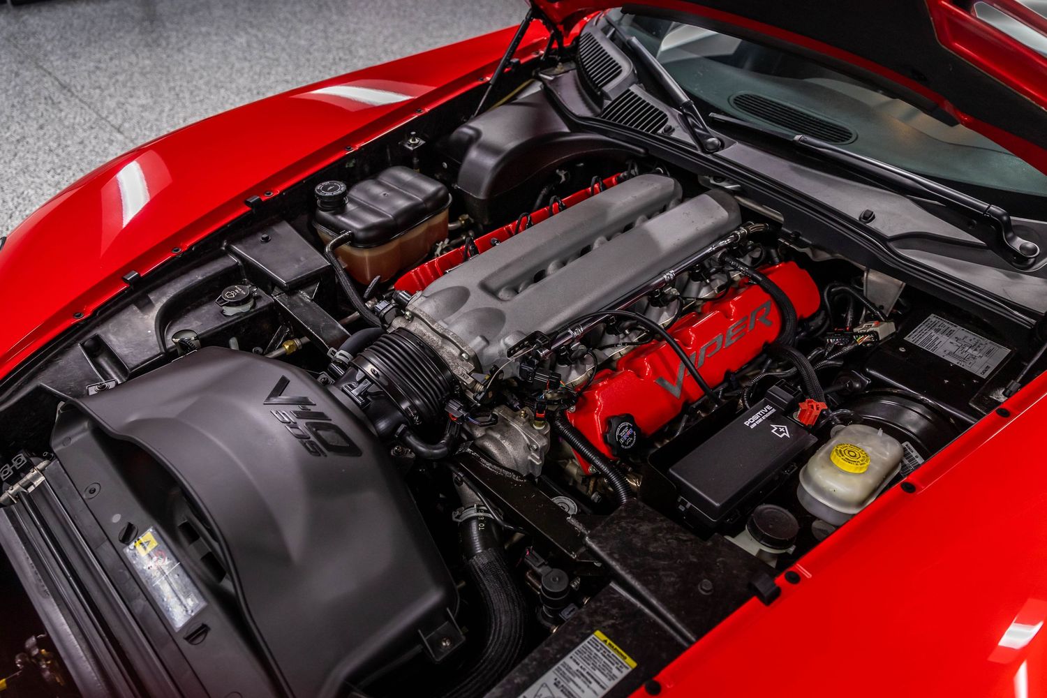 Close-up view of a red car's engine bay showing various mechanical components and engine parts.