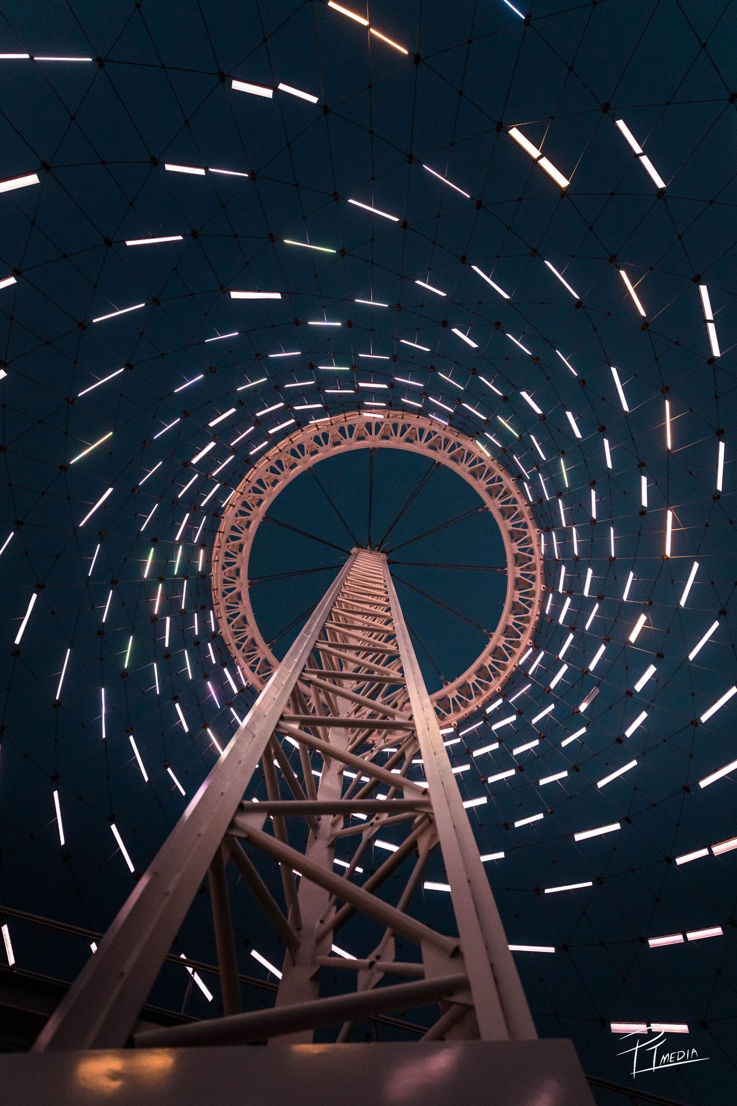 Long exposure photograph captures circular light trails around a towering roller coaster structure against a dark night sky.