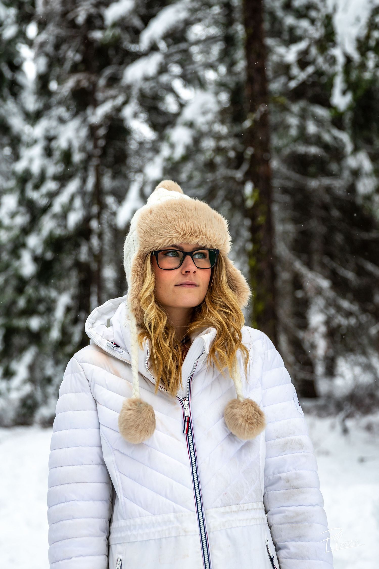 Person in white puffer coat with fur trim hood poses in snowy winter forest setting.