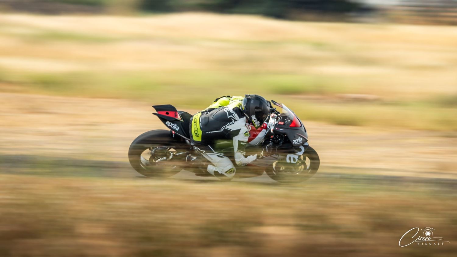 A racing motorcycle speeds around a track, captured with motion blur emphasizing high speed in an outdoor racing event.