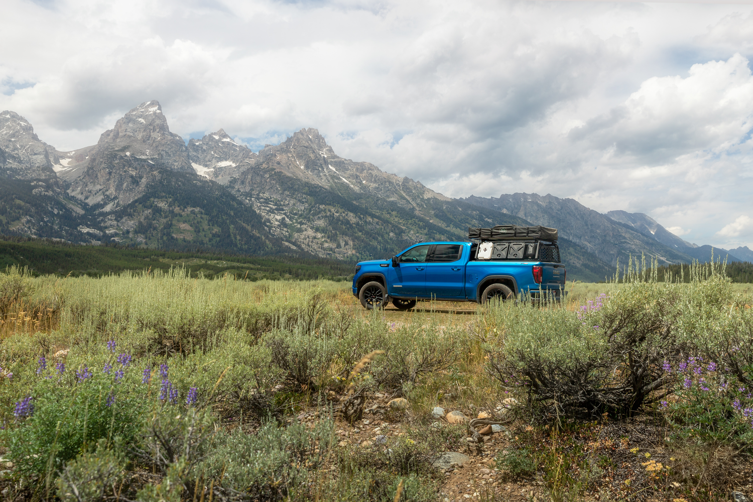 Blue GMC Sierra parked in meadow with Grand Teton mountains in background.