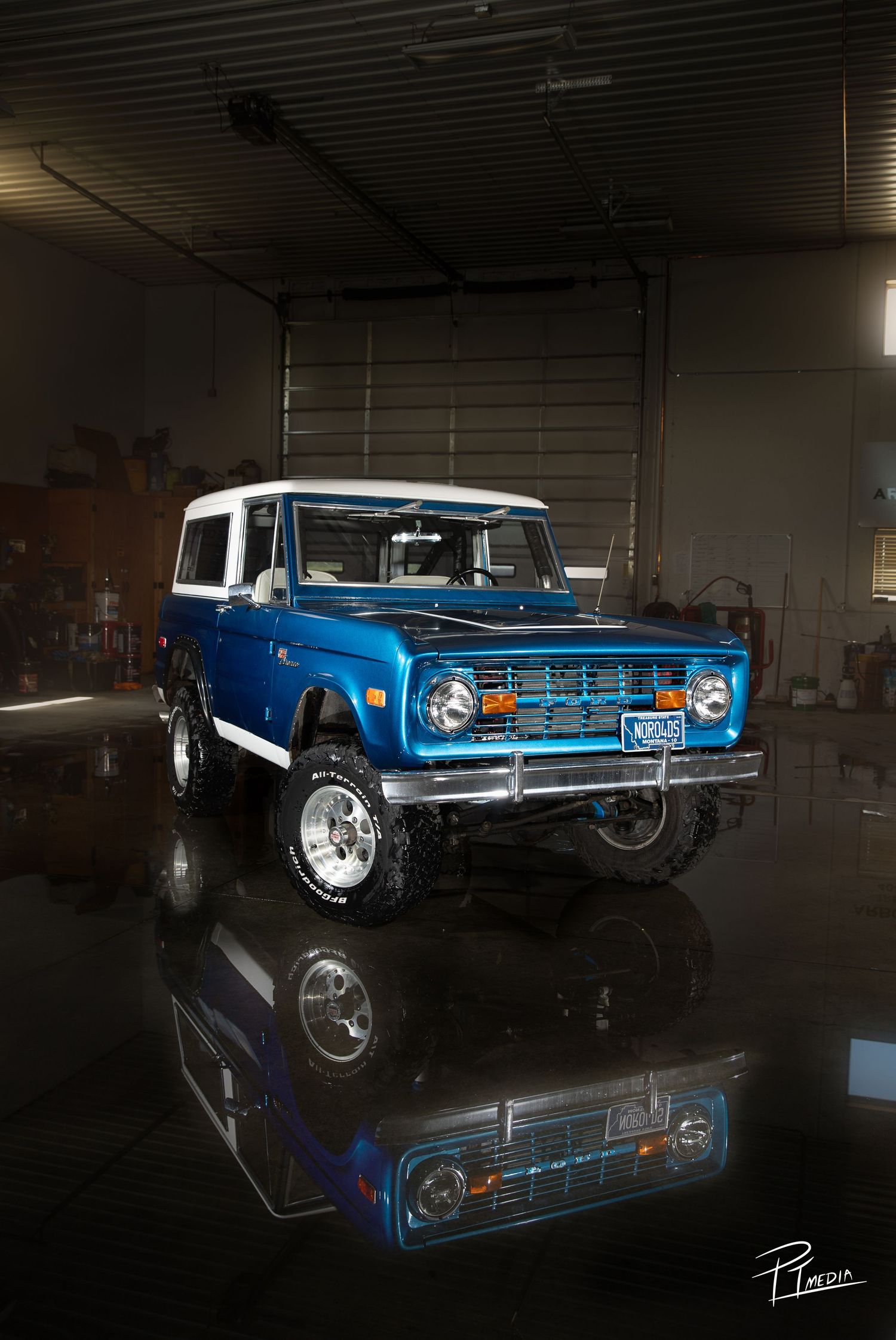 A vintage blue Chevrolet Nova SS muscle car photographed in a dark garage with dramatic lighting and reflective floor.