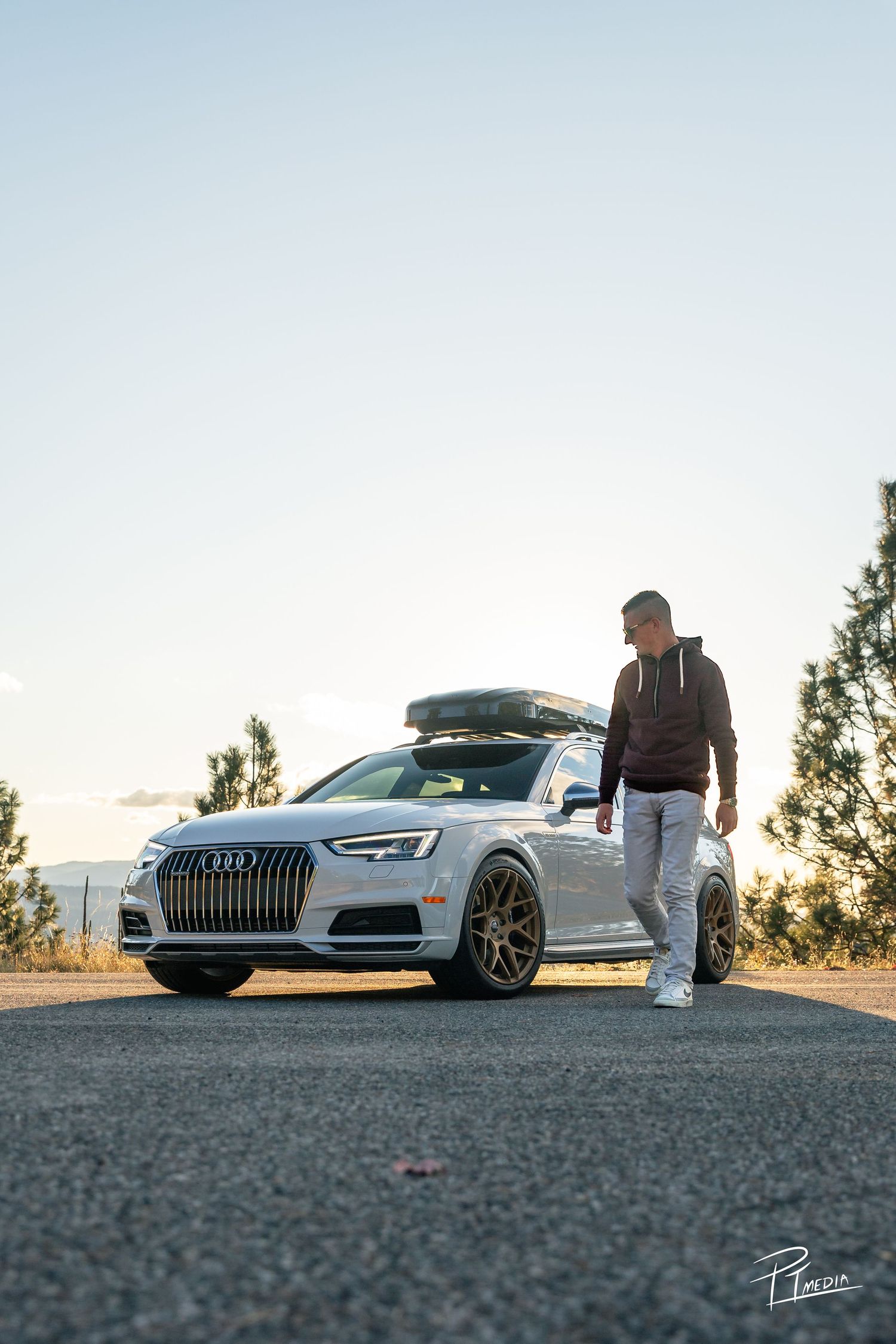 A lowered silver Audi with roof cargo box parked on a scenic mountain road at sunset.