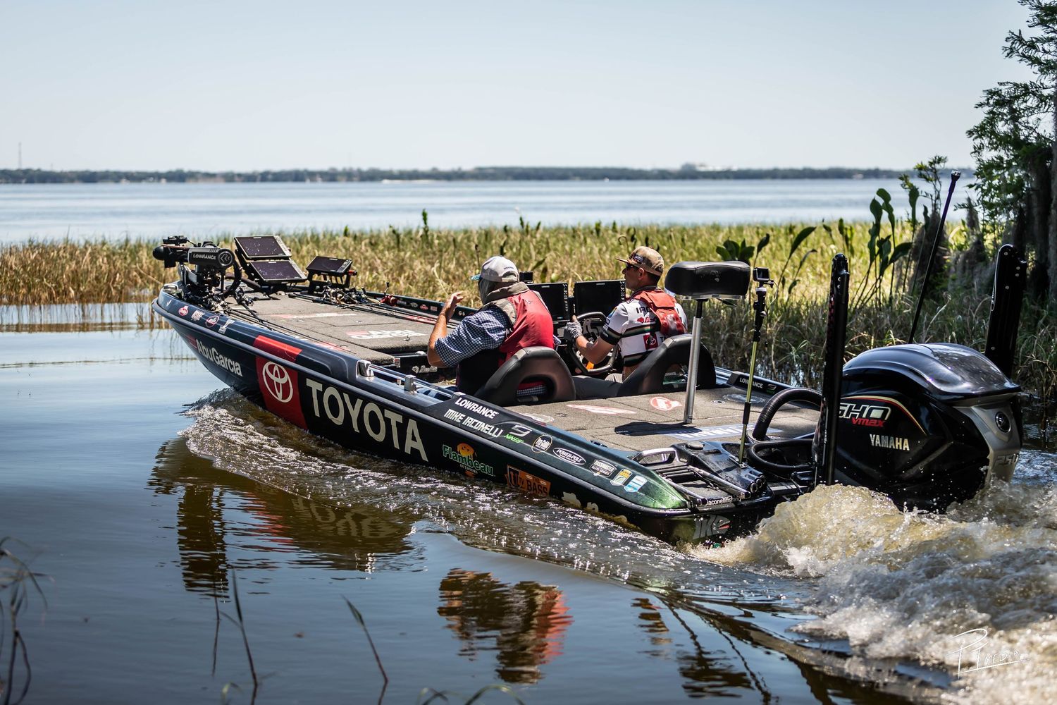 A series of boats navigating through marsh waters with splashing wakes in an outdoor recreational setting.