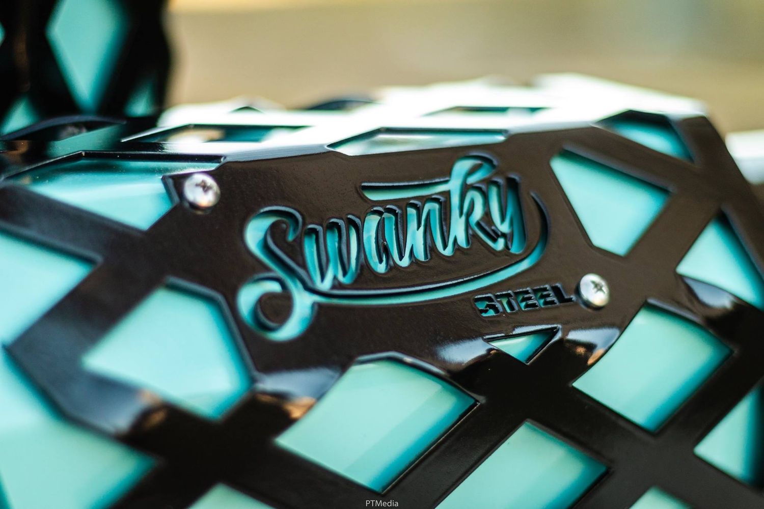 Close-up macro photography of black skateboard wheels and trucks against a turquoise background.