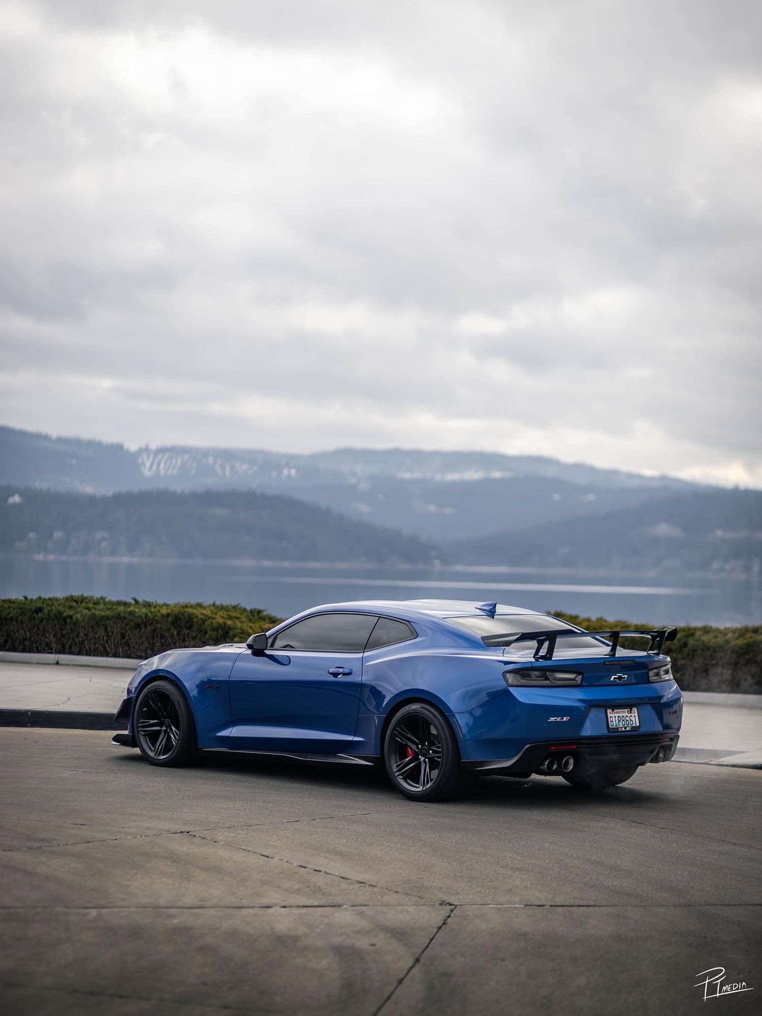 A blue Chevrolet Camaro ZL1 parked on a scenic overlook with mountains and water in the background.