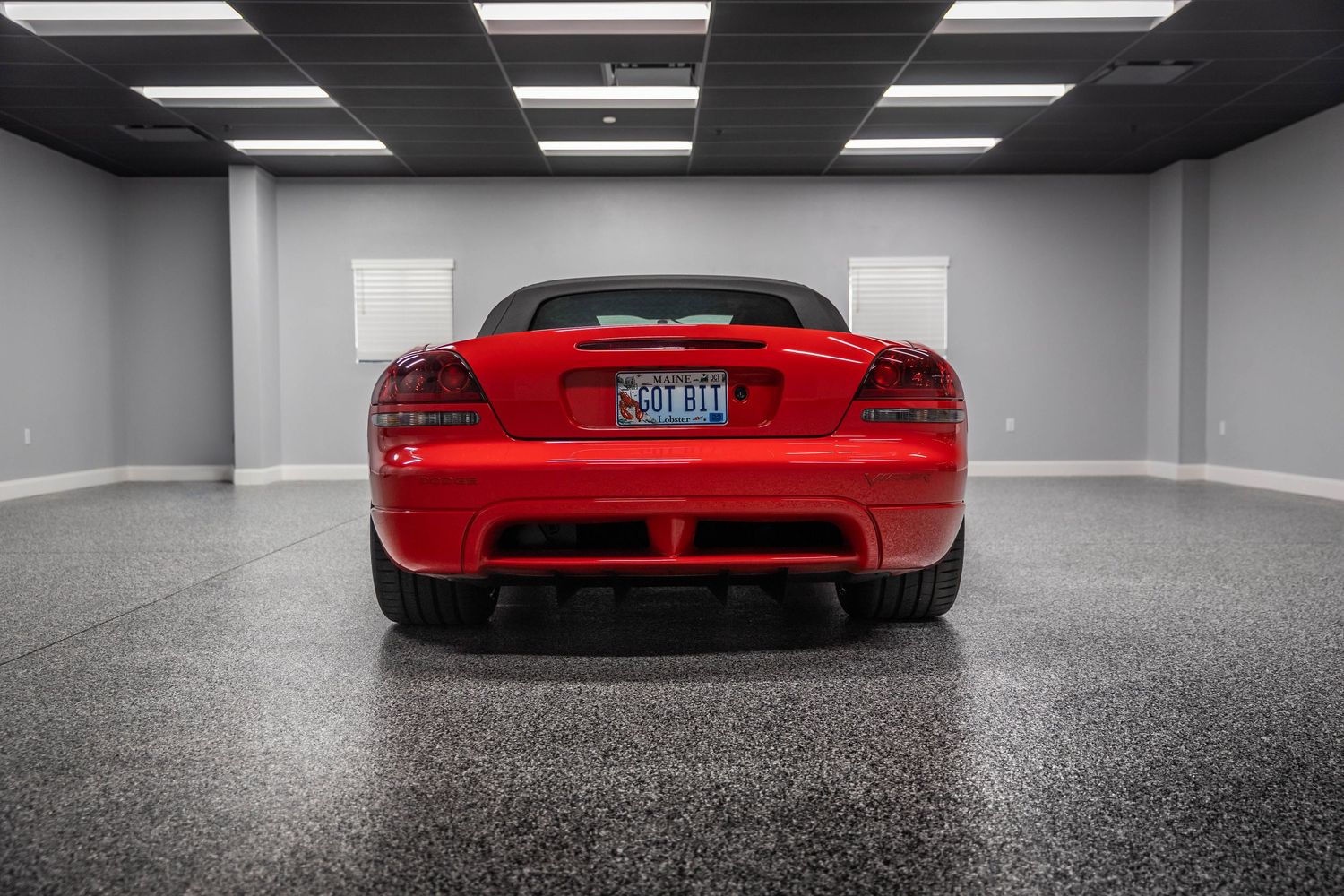 Rear view of a bright red Dodge Viper sports car in a sleek gray garage with fluorescent lighting.