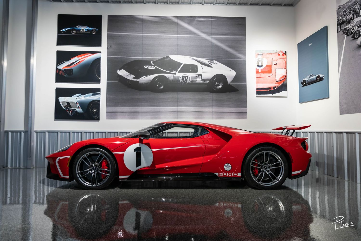 A sleek red sports car with racing number 1 displayed in an automotive gallery with black and white photographs.