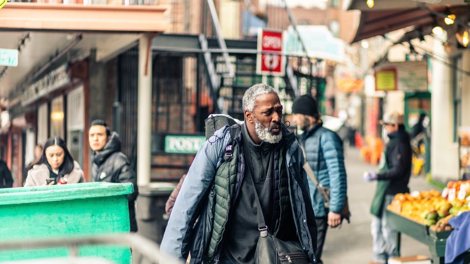 People walk past colorful storefronts and shops on a busy urban street in winter.