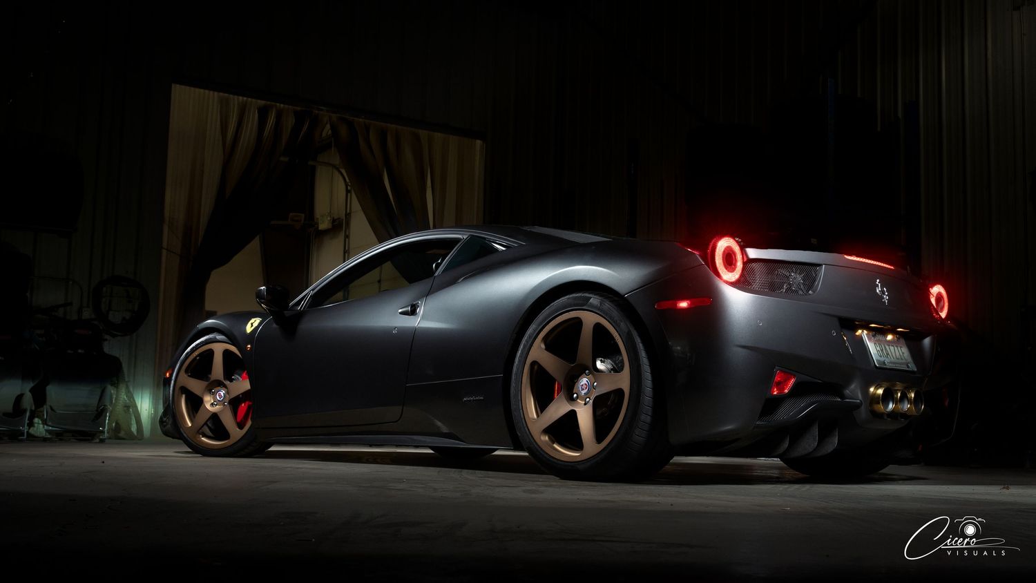 A sleek grey Ferrari 458 photographed in a dramatic low-light setting with glowing red taillights in Coeur d' Alene, Idaho
