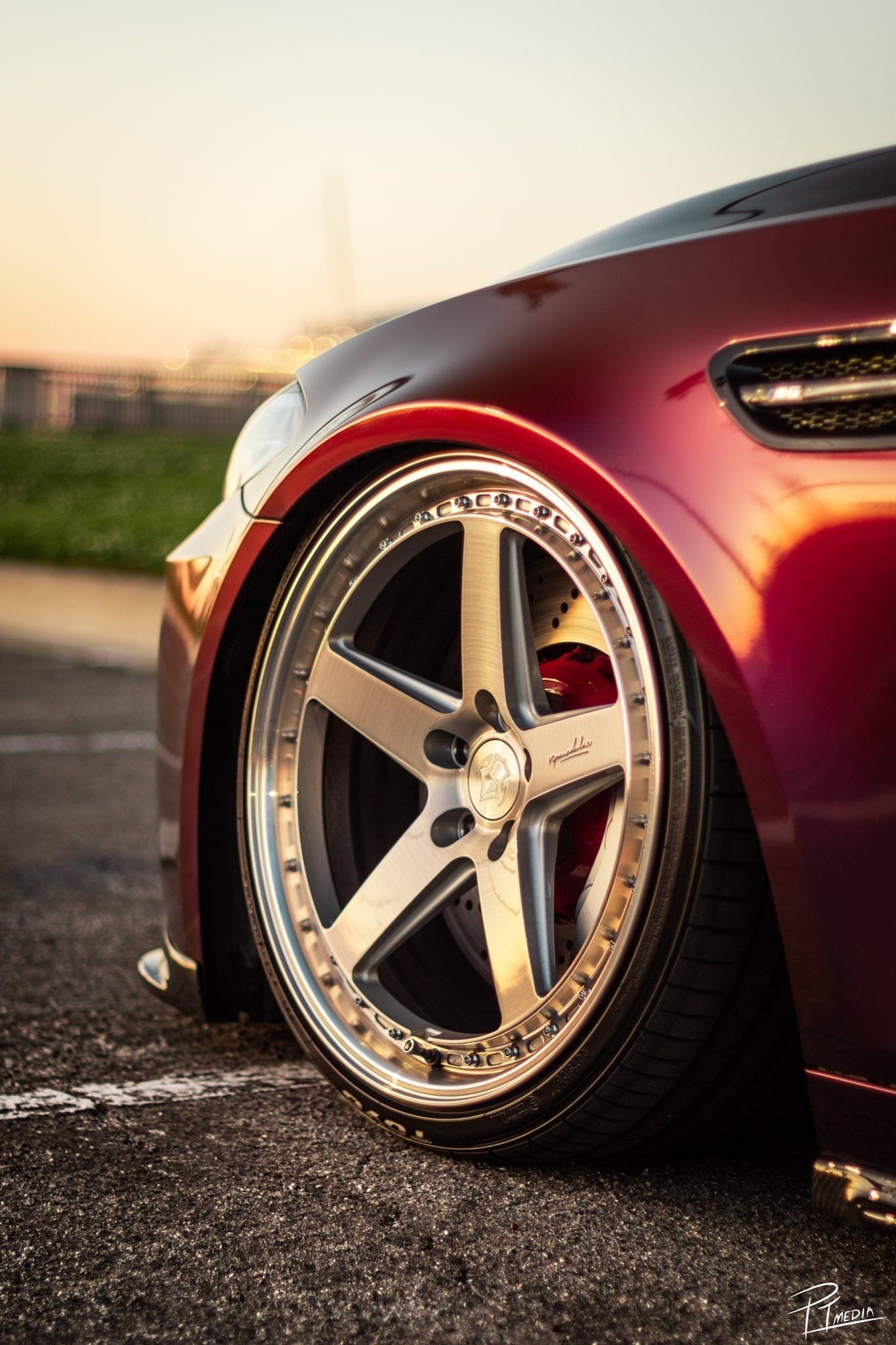 Close-up shots of a burgundy car's custom wheels featuring five-spoke silver rims with chrome accents against asphalt at sunset.