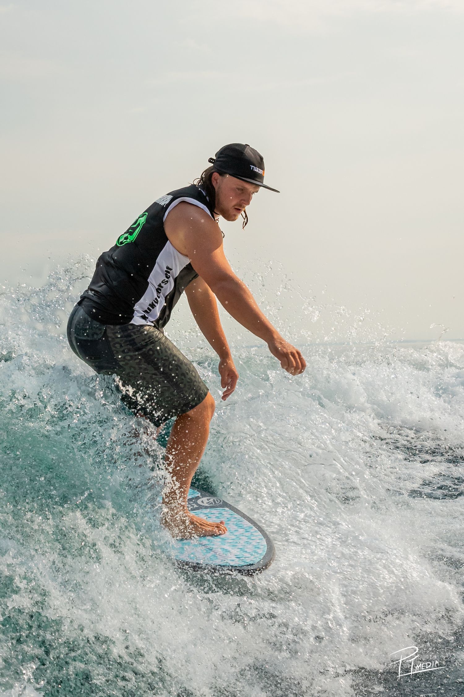 A surfer rides a wave while wakeboarding, creating dynamic splashes in the turquoise ocean water.