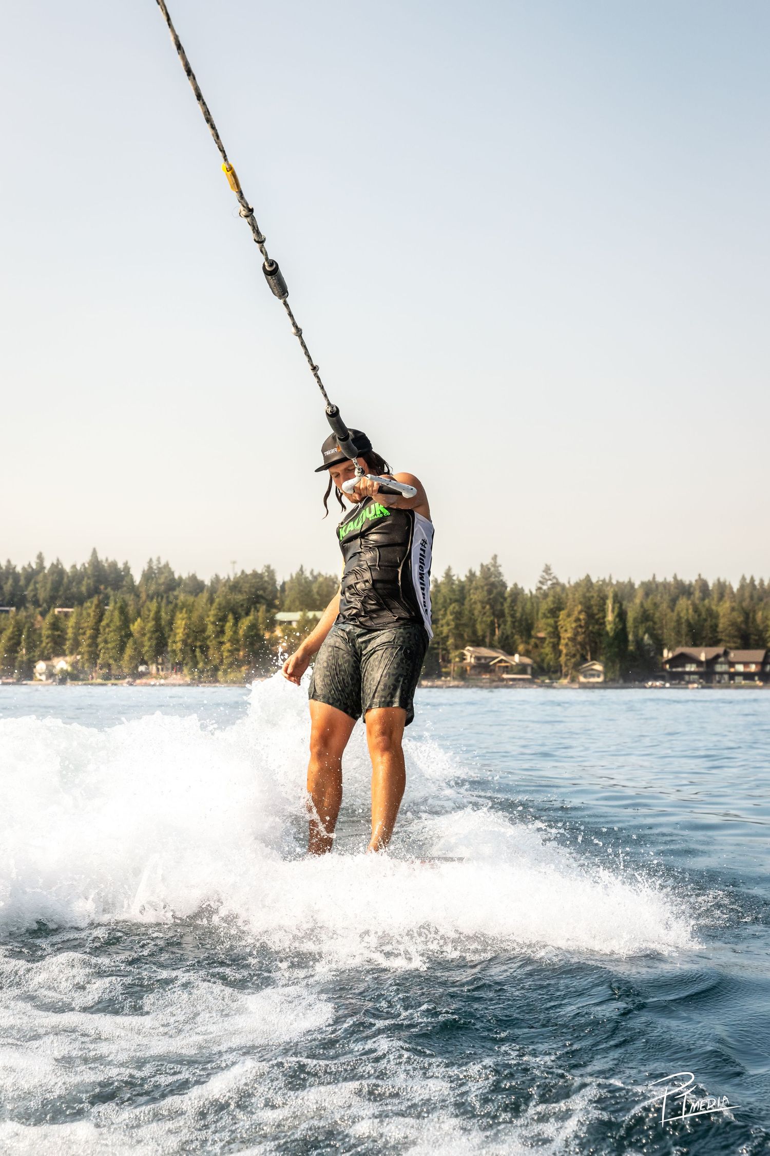 A sequence of action shots showing a wakeboarder gliding and splashing across the lake surface with pine trees in background.