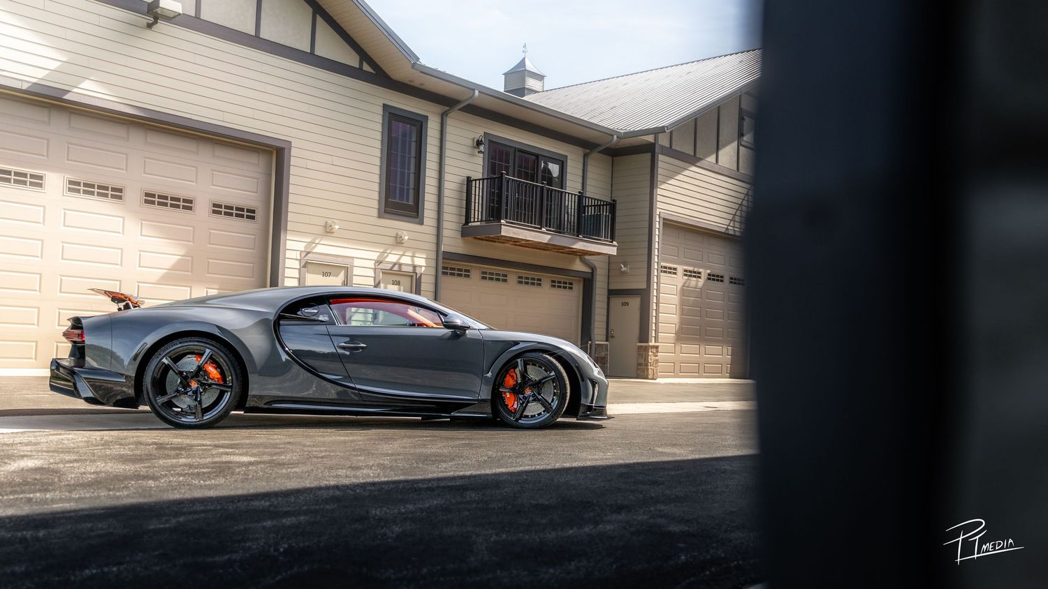 Black Bugatti Chiron Sport supercar with orange accents parked in front of residential garages.
