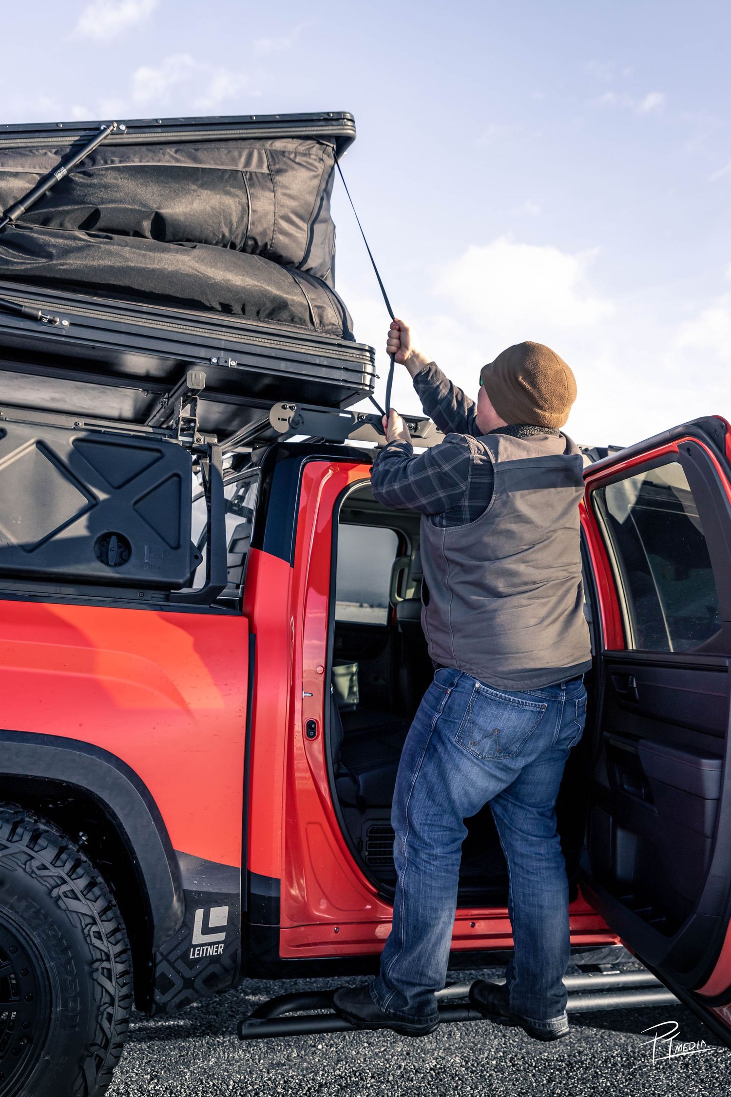 Person loading cargo into the back of a customized red Toyota pickup truck.