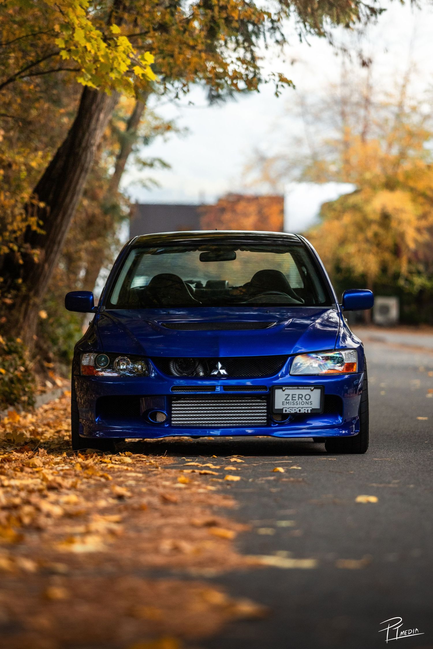 Low stance blue Honda Civic coupe with aftermarket modifications parked on autumn leaf-covered road at sunset.