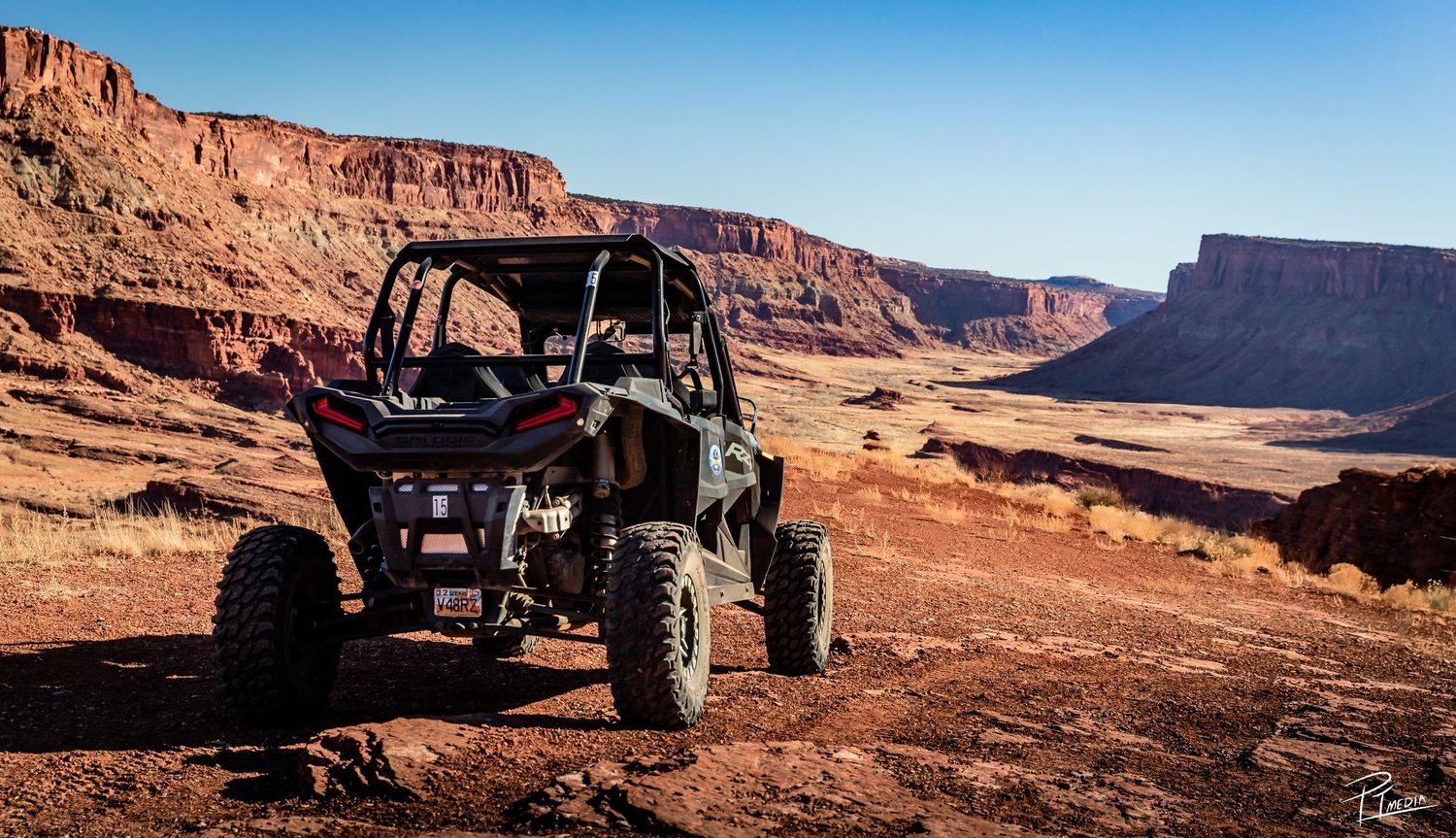Off-road vehicles traverse rugged red rock terrain in Moab's scenic desert landscape under clear blue skies.