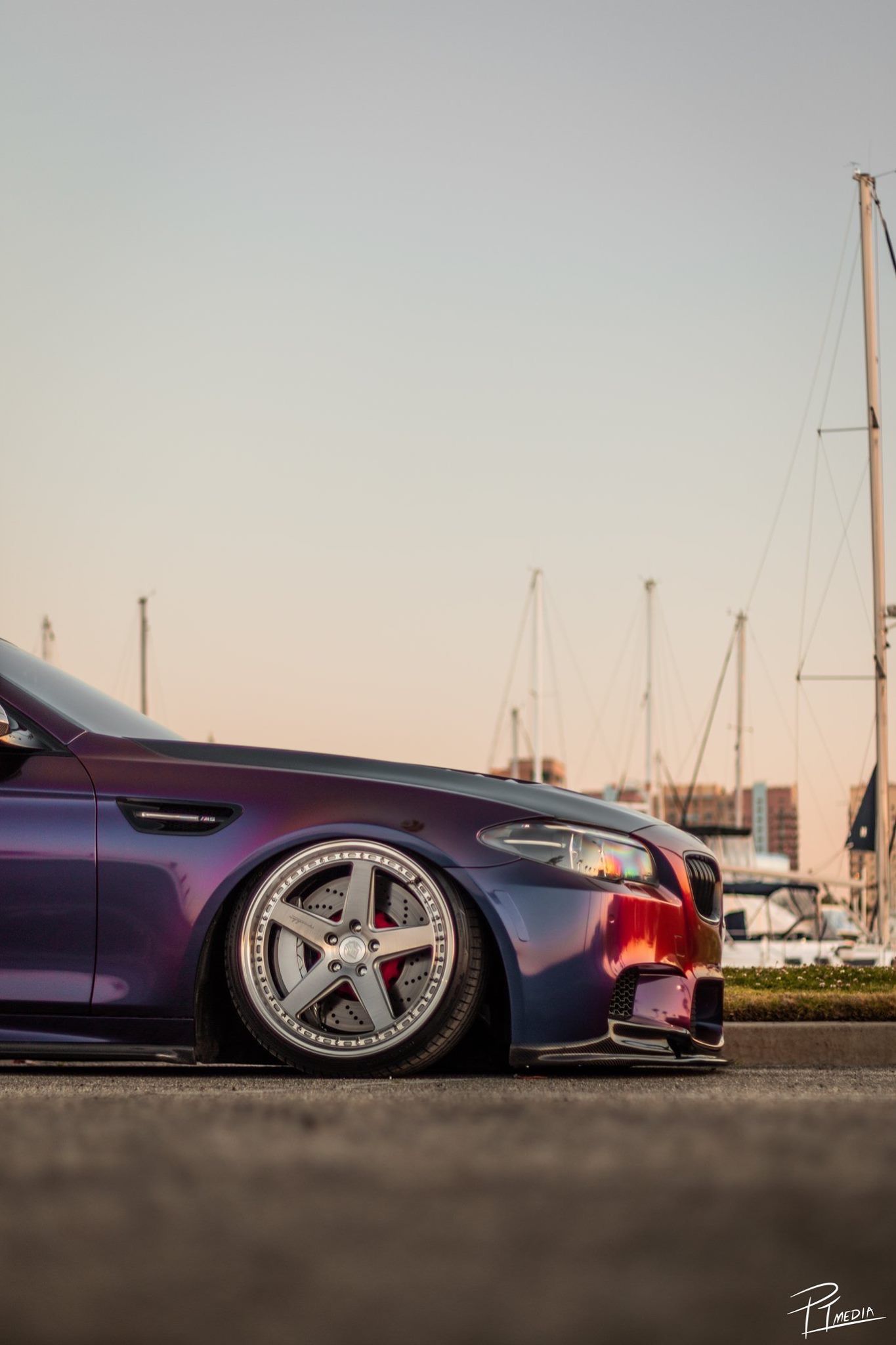 Low angle view of a purple sports car with custom wheels parked at a marina during sunset.