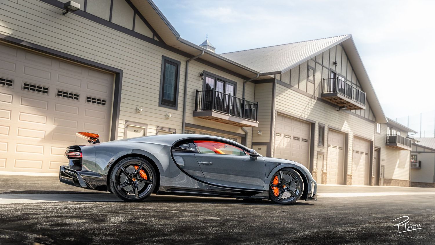 A panoramic view of luxury sports cars parked in front of modern residential buildings and garages.