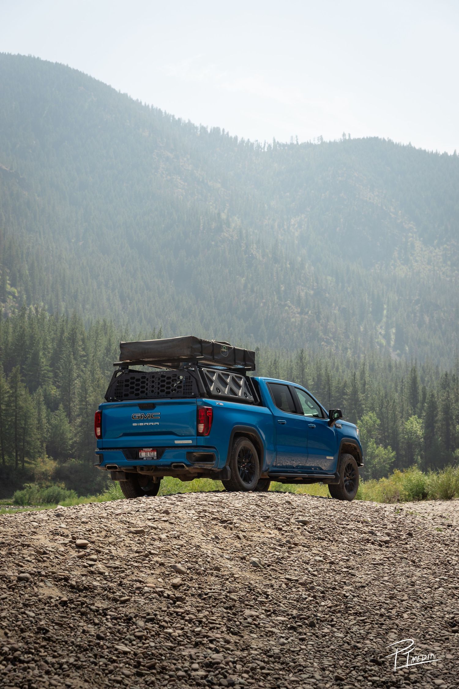 Blue Ford Ranger pickup truck parked on rocky overlook with forested mountain landscape in the background.