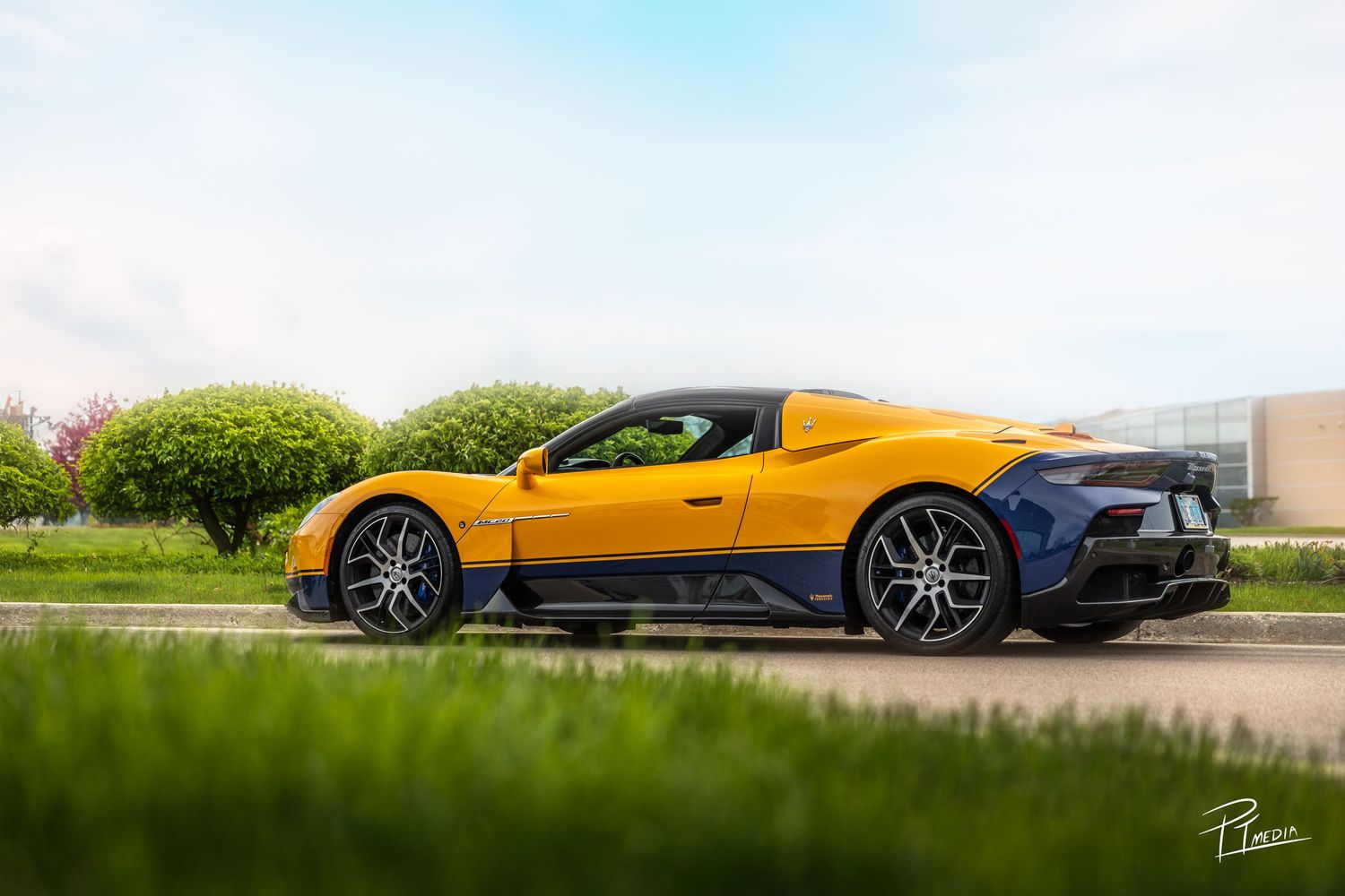 Low-angle view of a bright yellow sports car against a blue sky and green landscape backdrop.