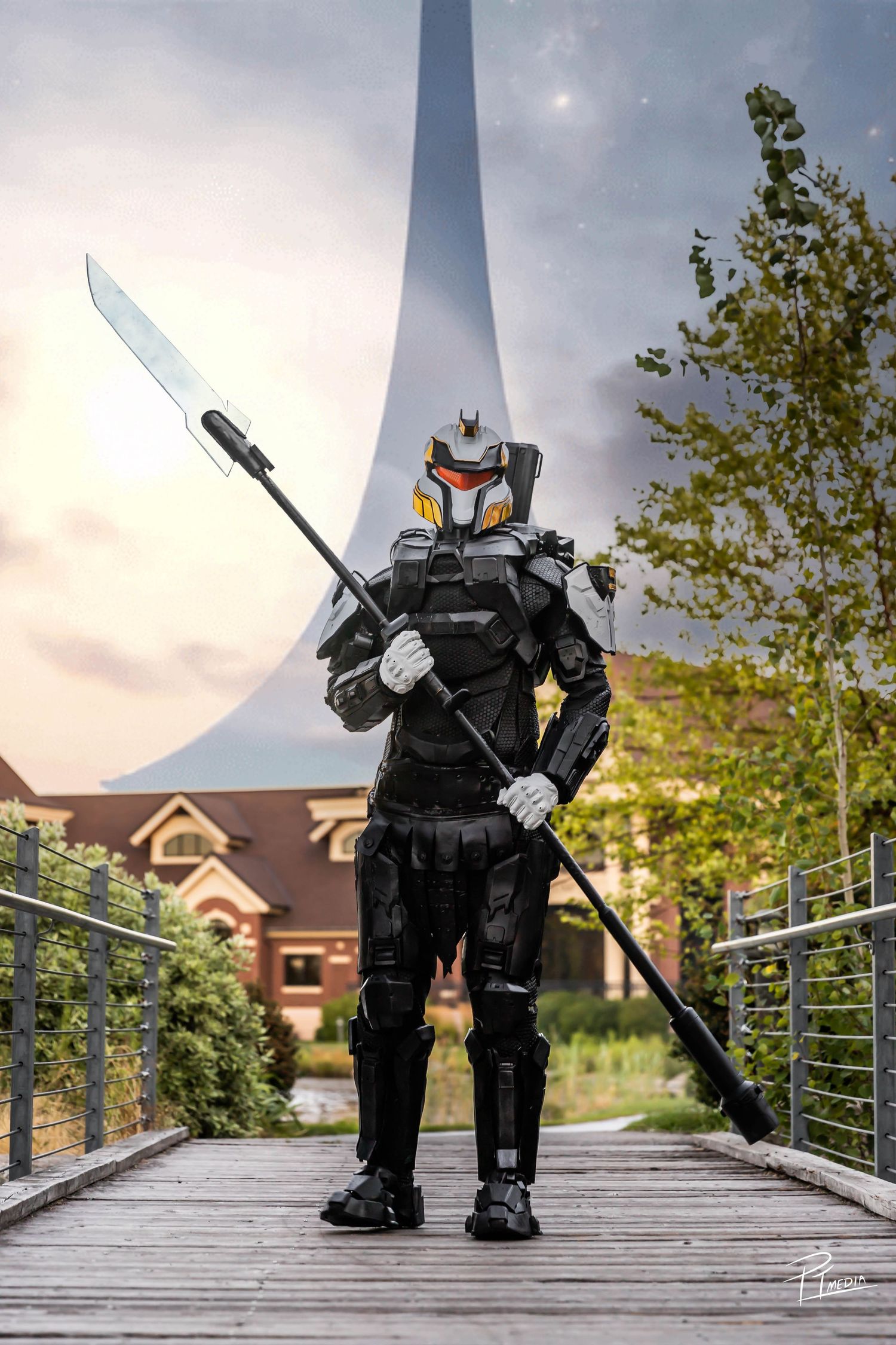 Cosplay figure in black armor and helmet poses dramatically on a wooden bridge during sunset.