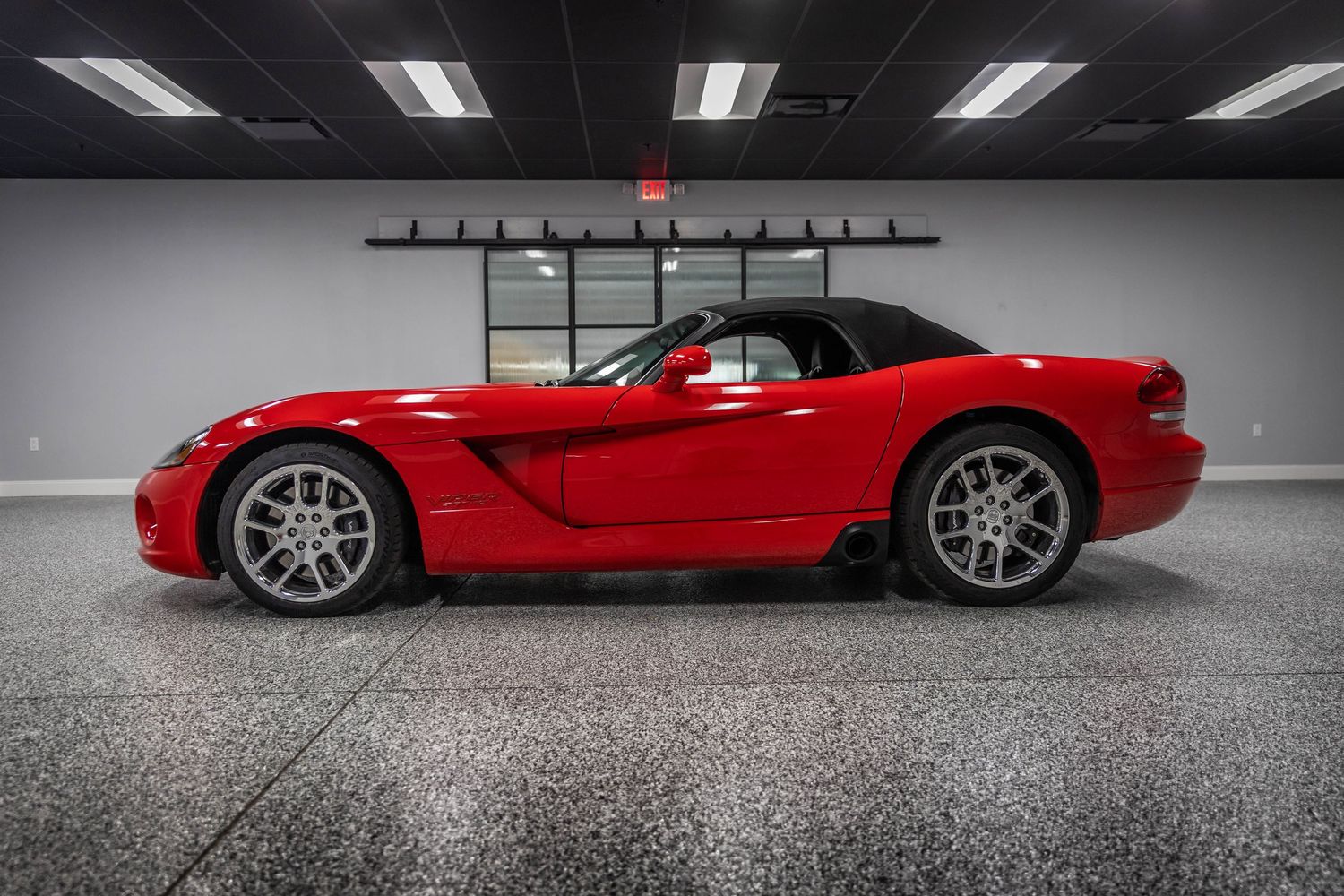 A bright red Dodge Viper sports car with silver wheels sits in a sleek garage with fluorescent lighting.