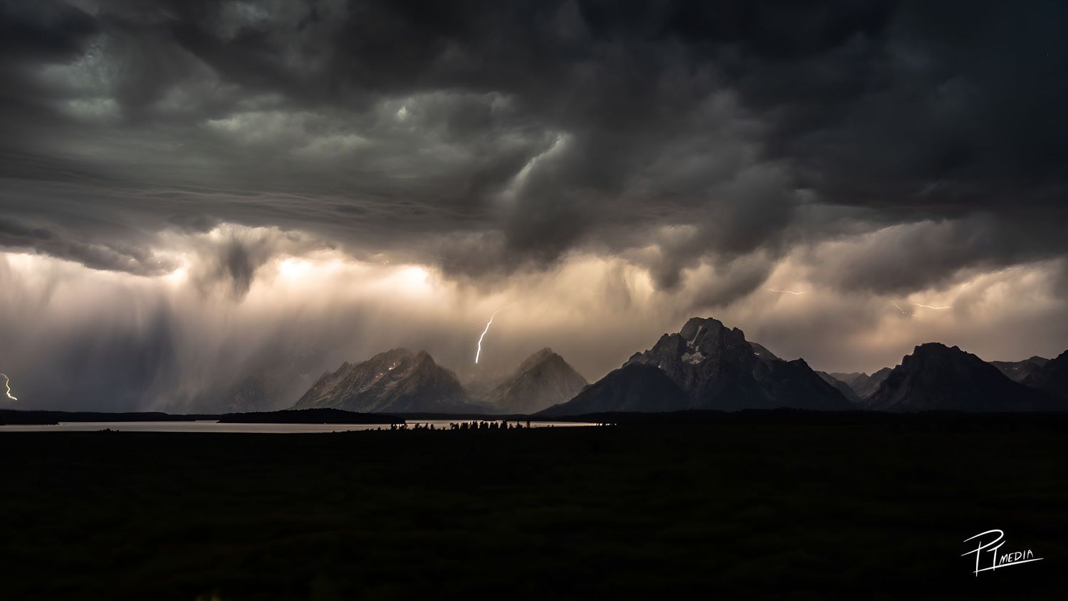 Dramatic panoramic landscape of dark storm clouds rolling over mountains and valleys at sunset.