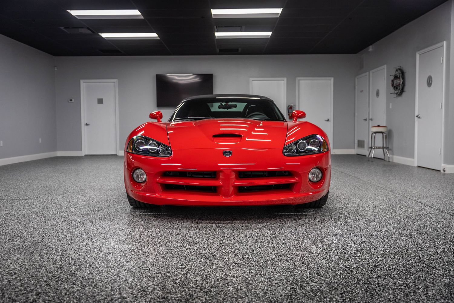 A bright red Dodge Viper sports car parked in a clean white garage with fluorescent lighting.