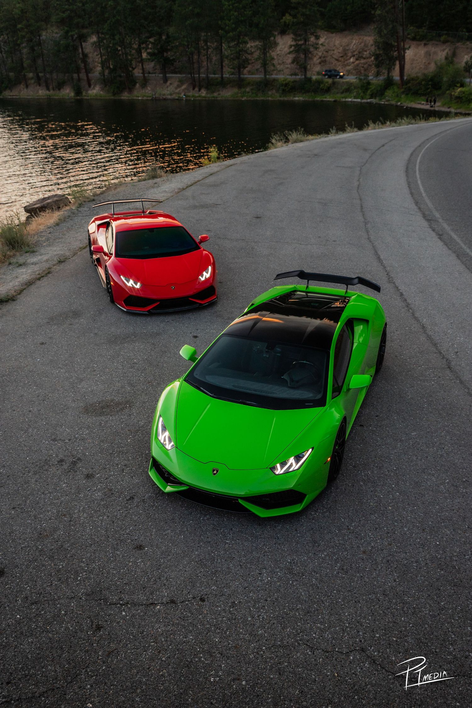 A red and green Lamborghini parked on a curved road next to a lake with lily pads.