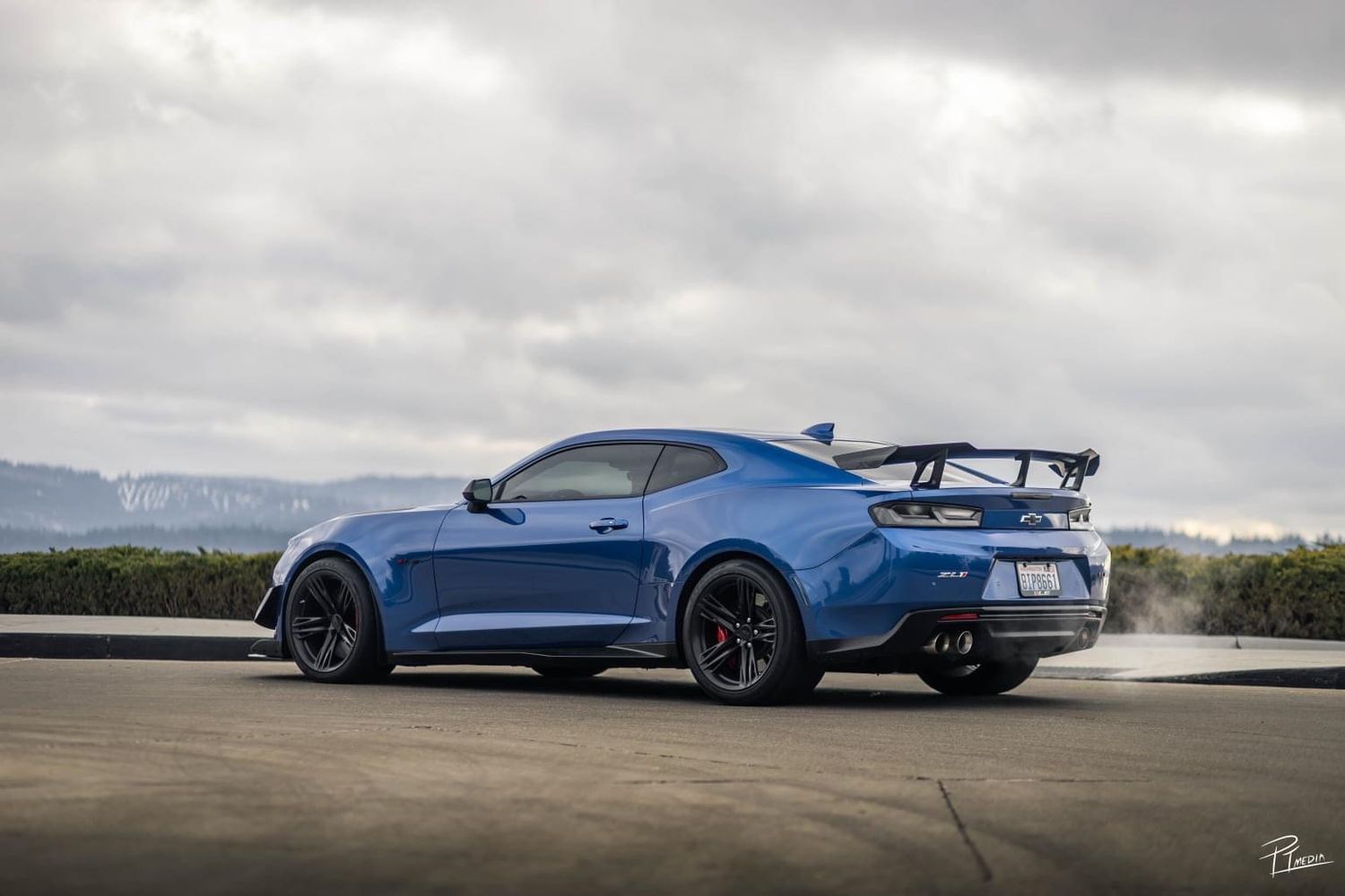 A blue sports car with an aggressive rear wing photographed from multiple angles on a cloudy day.