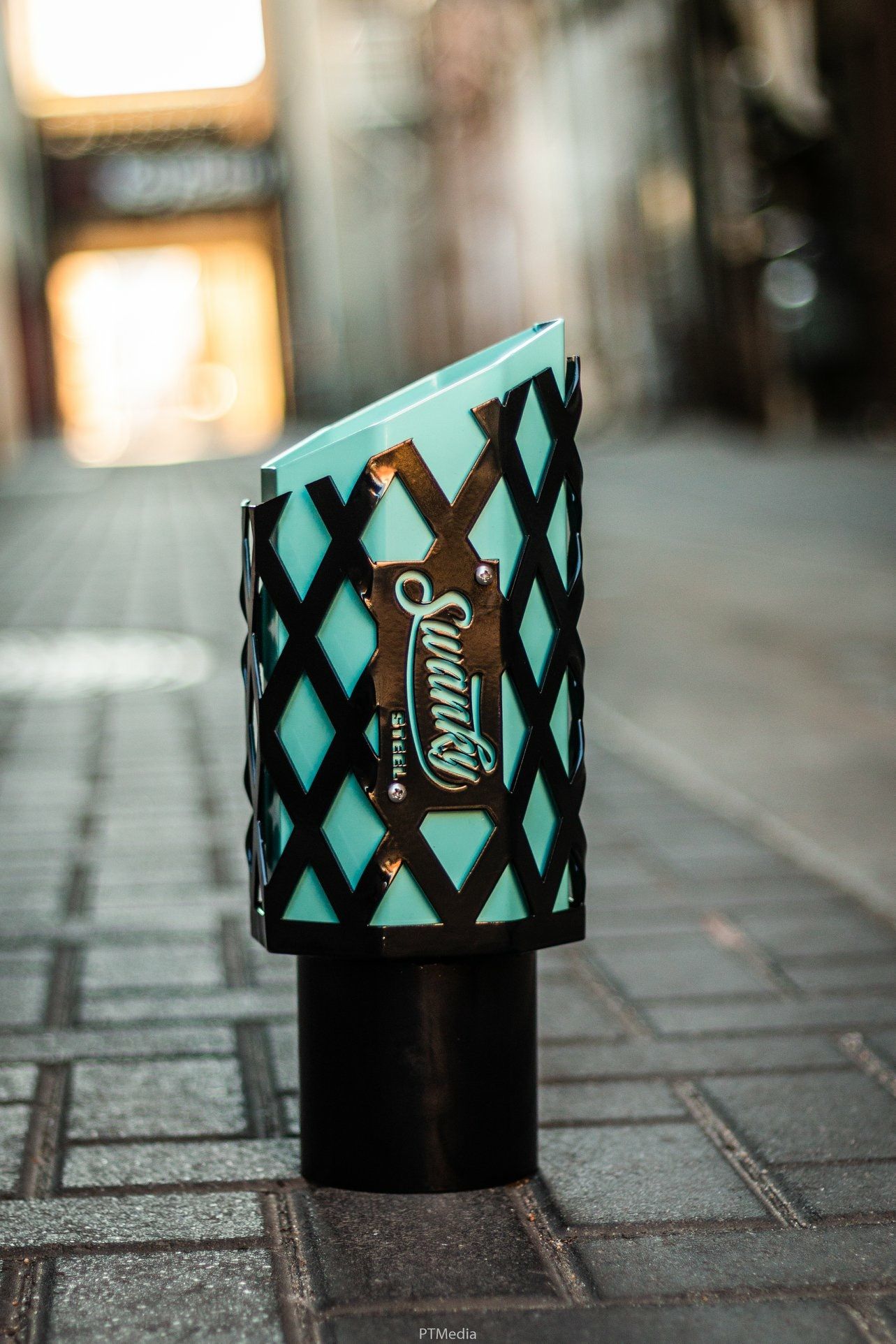 A row of disposable coffee cups with turquoise and black geometric patterns sitting on a cobblestone street.