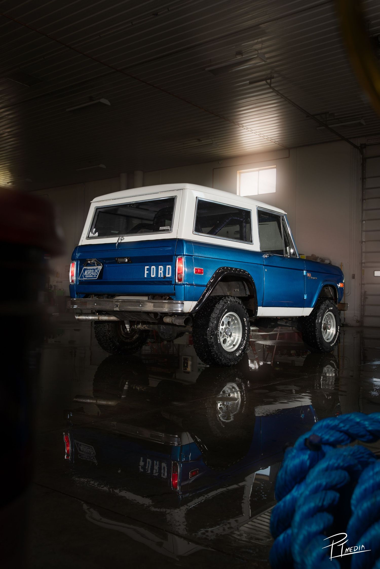 A blue Ford pickup truck with chrome wheels photographed in a dark garage with dramatic lighting and reflective surfaces.