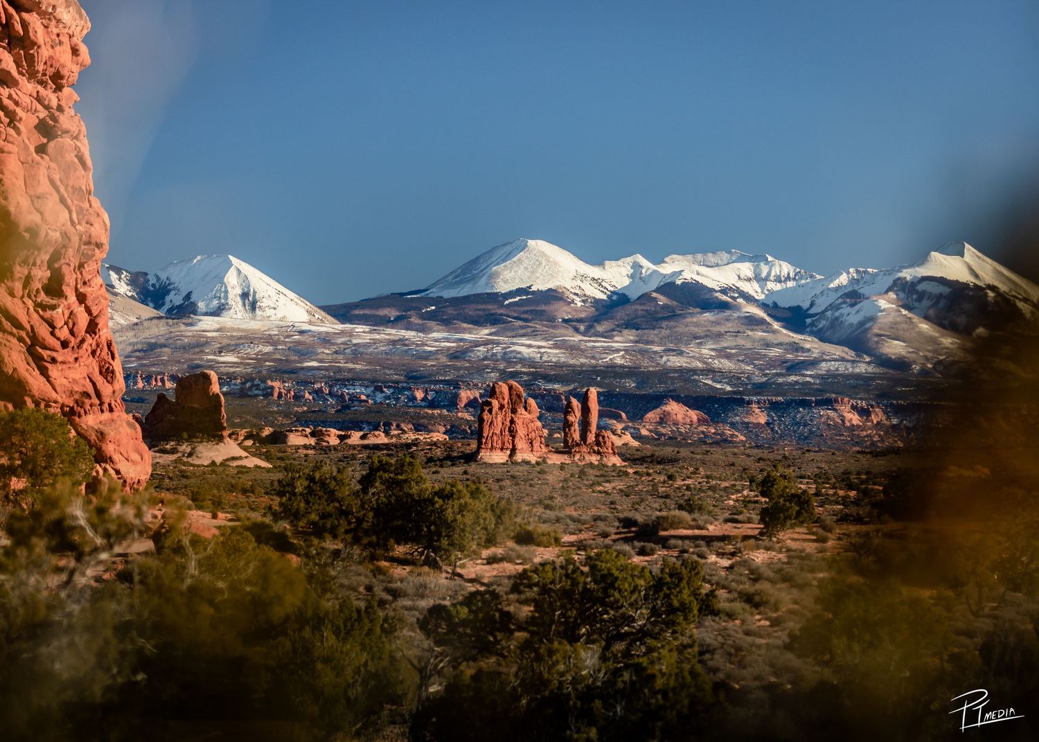 Panoramic view of snow-capped La Sal Mountains rising behind red rock formations in Arches National Park, Utah.