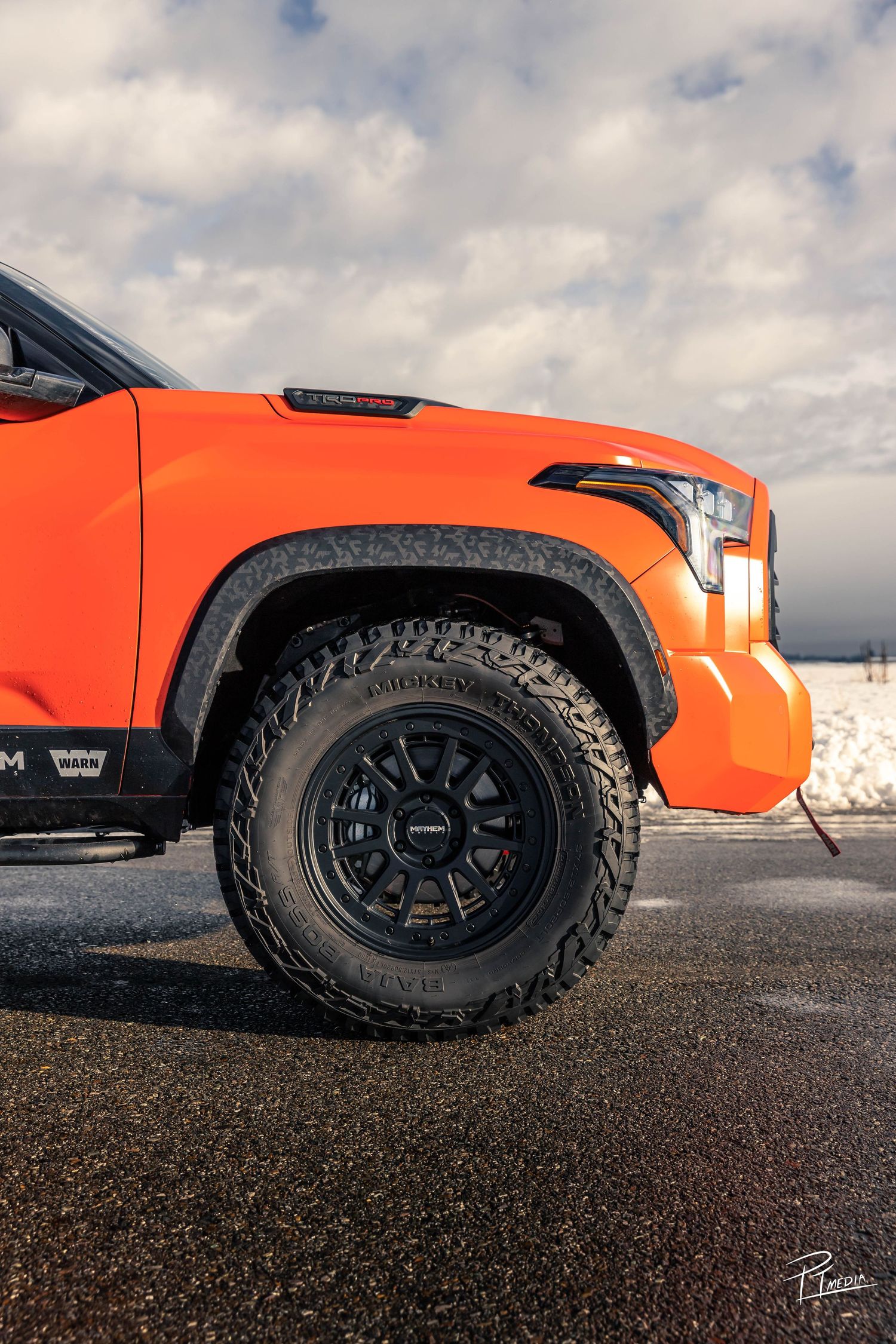 Close-up sequence showing orange off-road vehicle wheels and tires on black gravel terrain under cloudy skies.