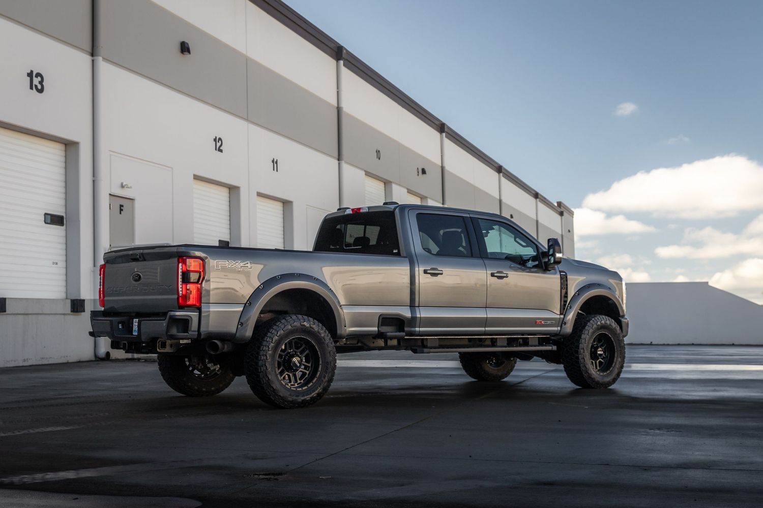 Custom lifted Ford F-250 Super Duty pickup truck with black wheels parked outside a commercial warehouse building.