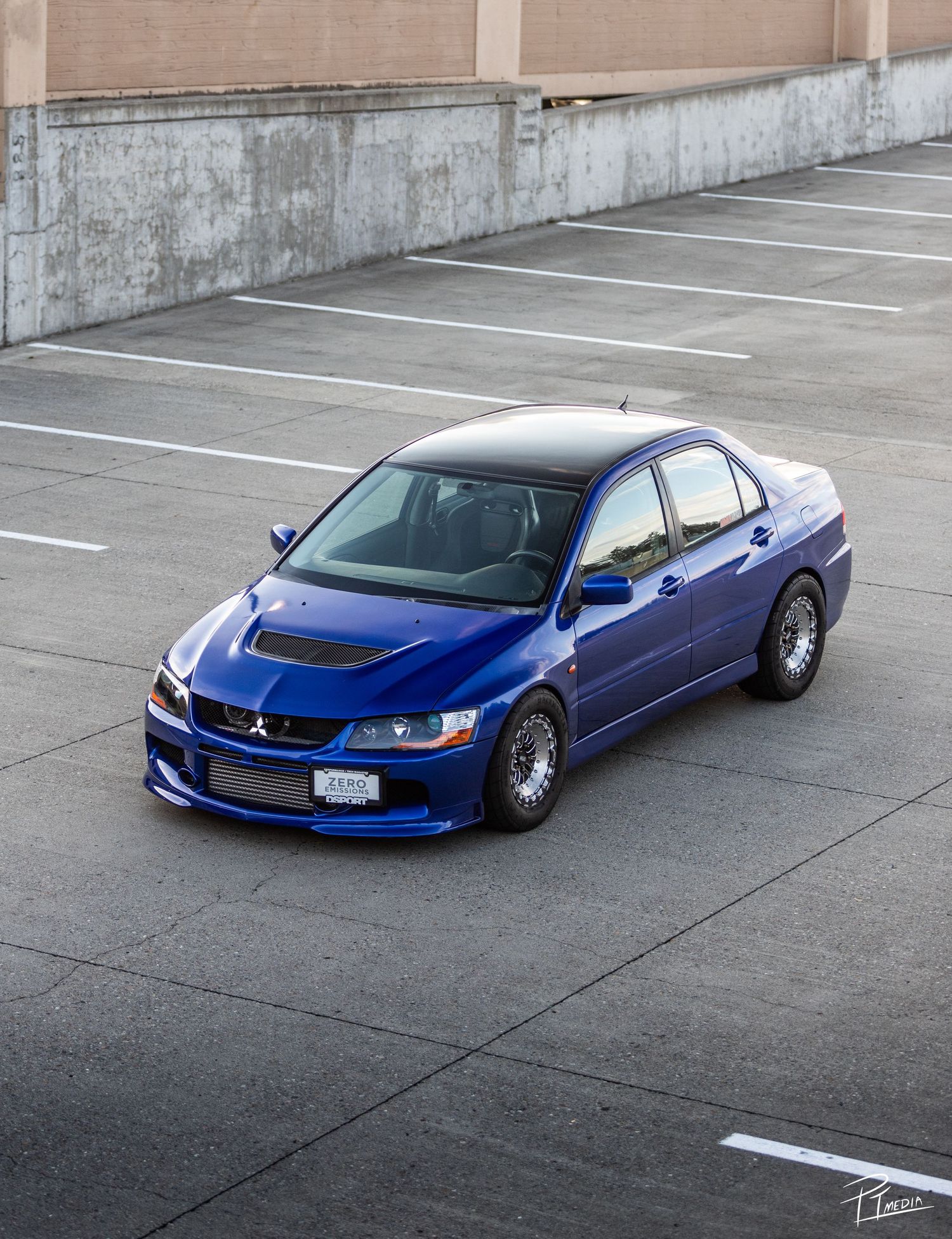 Modified blue Mitsubishi Lancer Evolution with custom wide body kit and lowered suspension parked in empty lot.