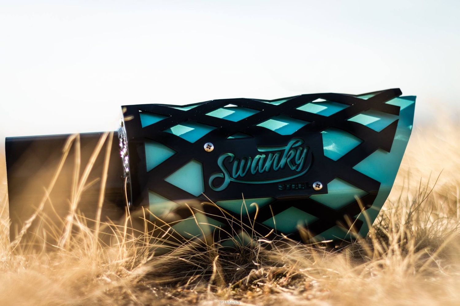 A turquoise and black geometric patterned Sunnies sunglasses case sits in dry grass during golden hour.