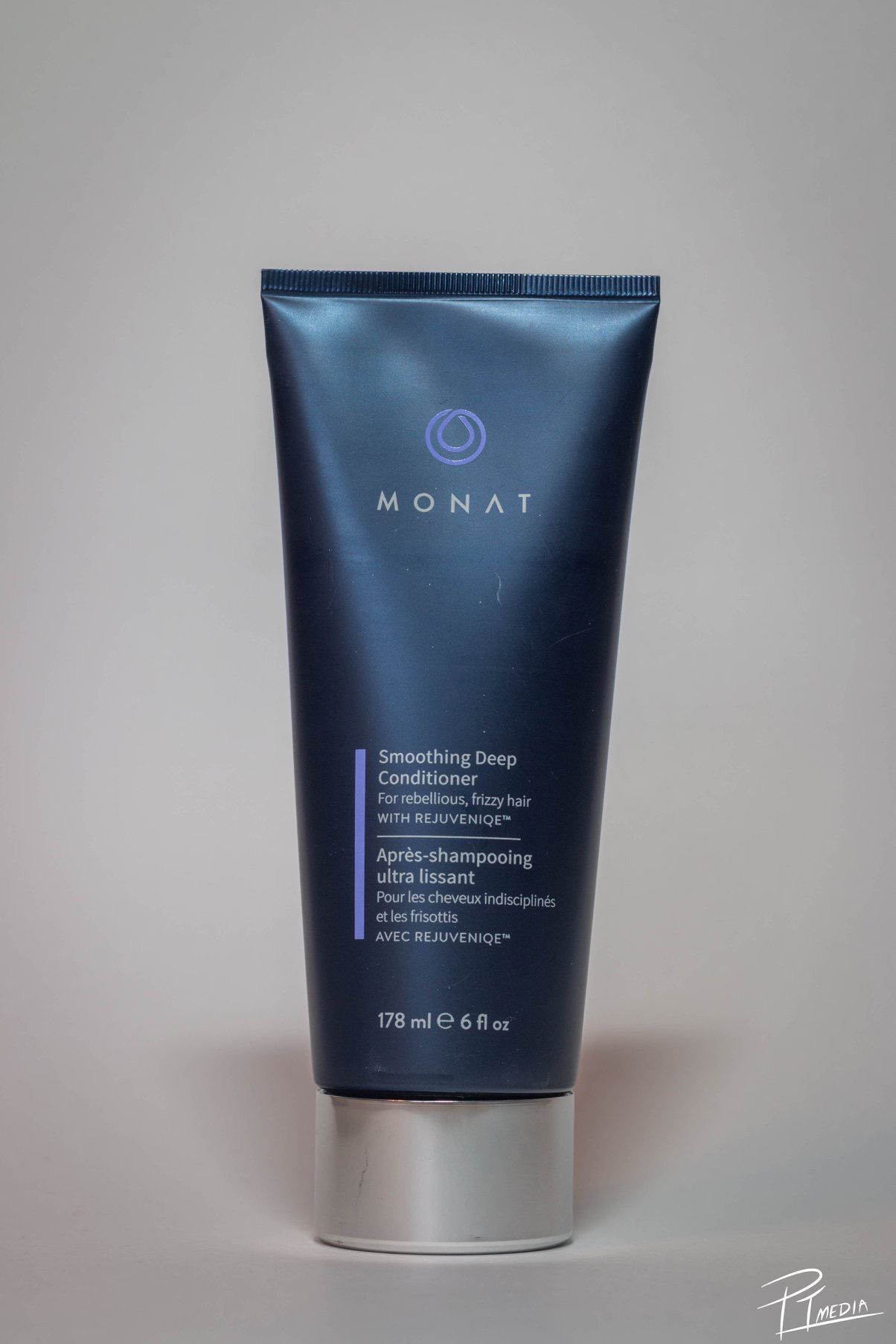 A navy blue cosmetic tube of Monat hair conditioning product shown from multiple angles against a light background.