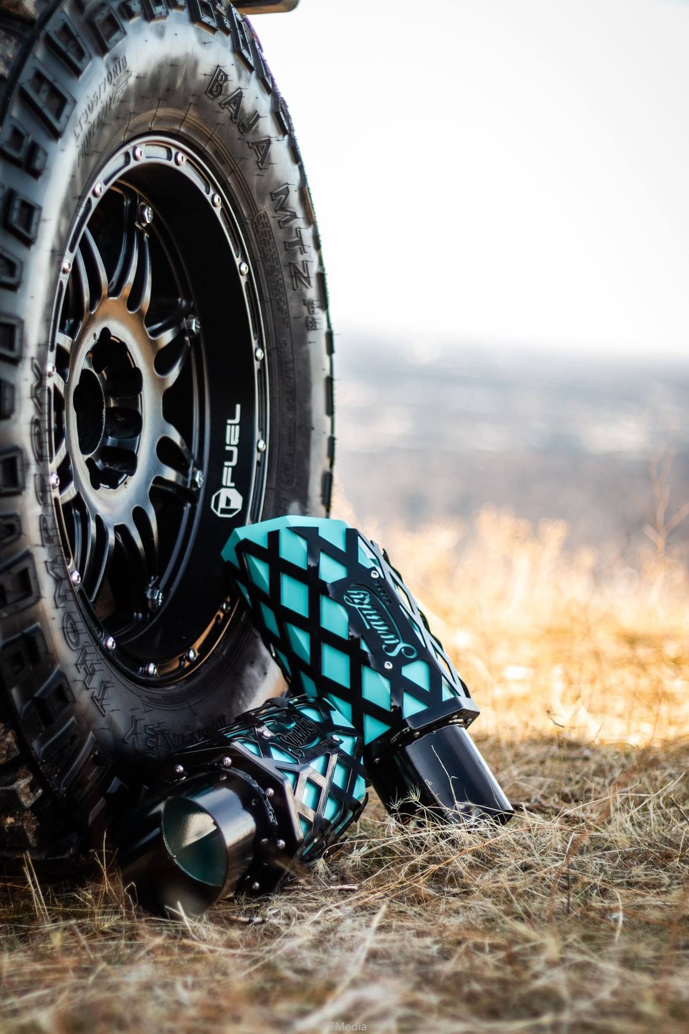 Close-up sequence of a black off-road tire with a teal and black checkered shoe against dry grass at sunset.
