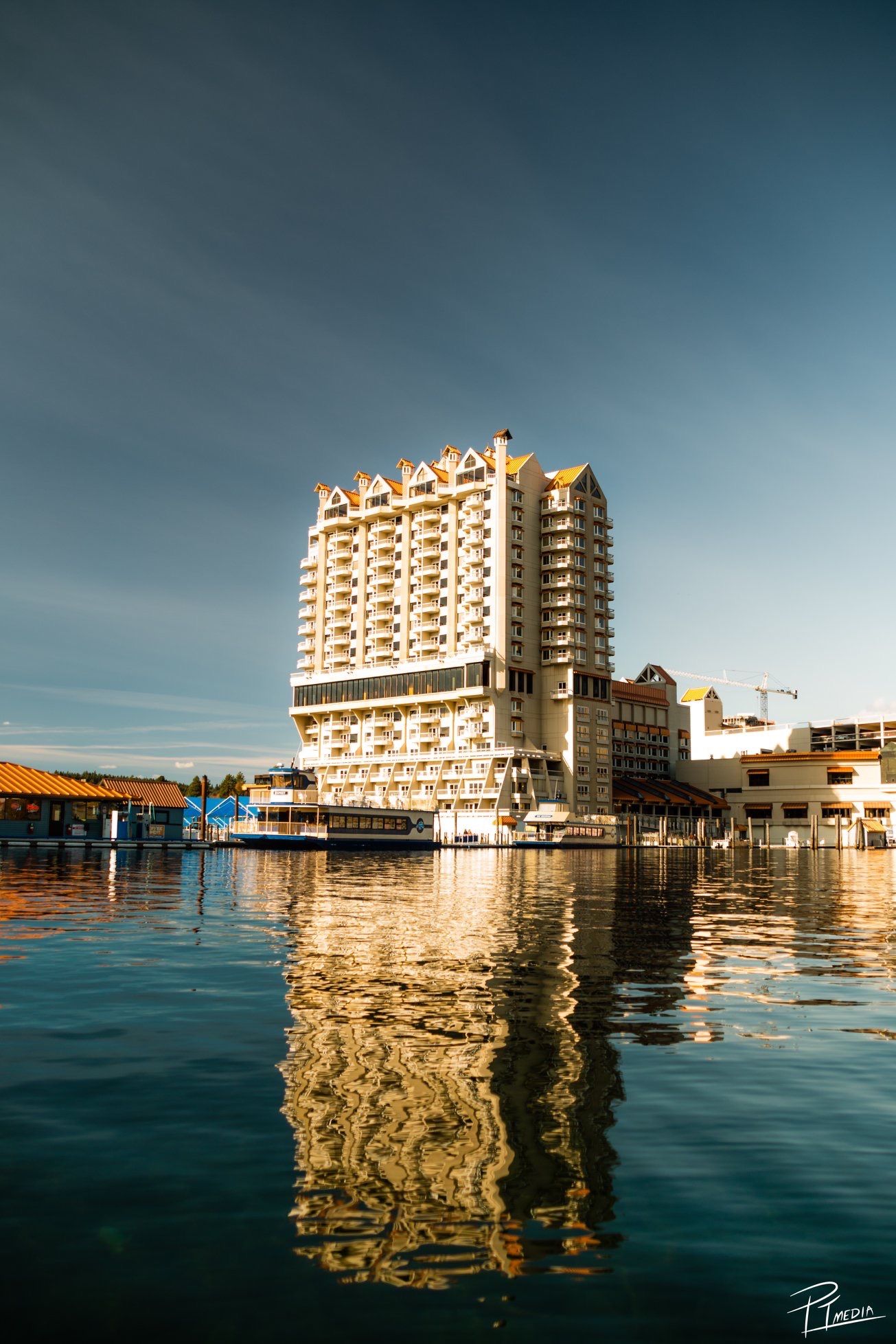 Panoramic view of waterfront hotels and buildings reflecting in calm blue waters during sunset.
