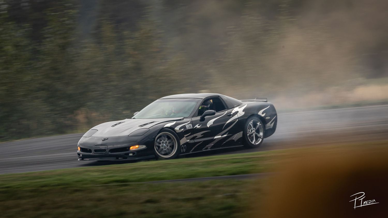 A black sports car races around a track with motion blur and tire smoke visible in the dramatic action shot.