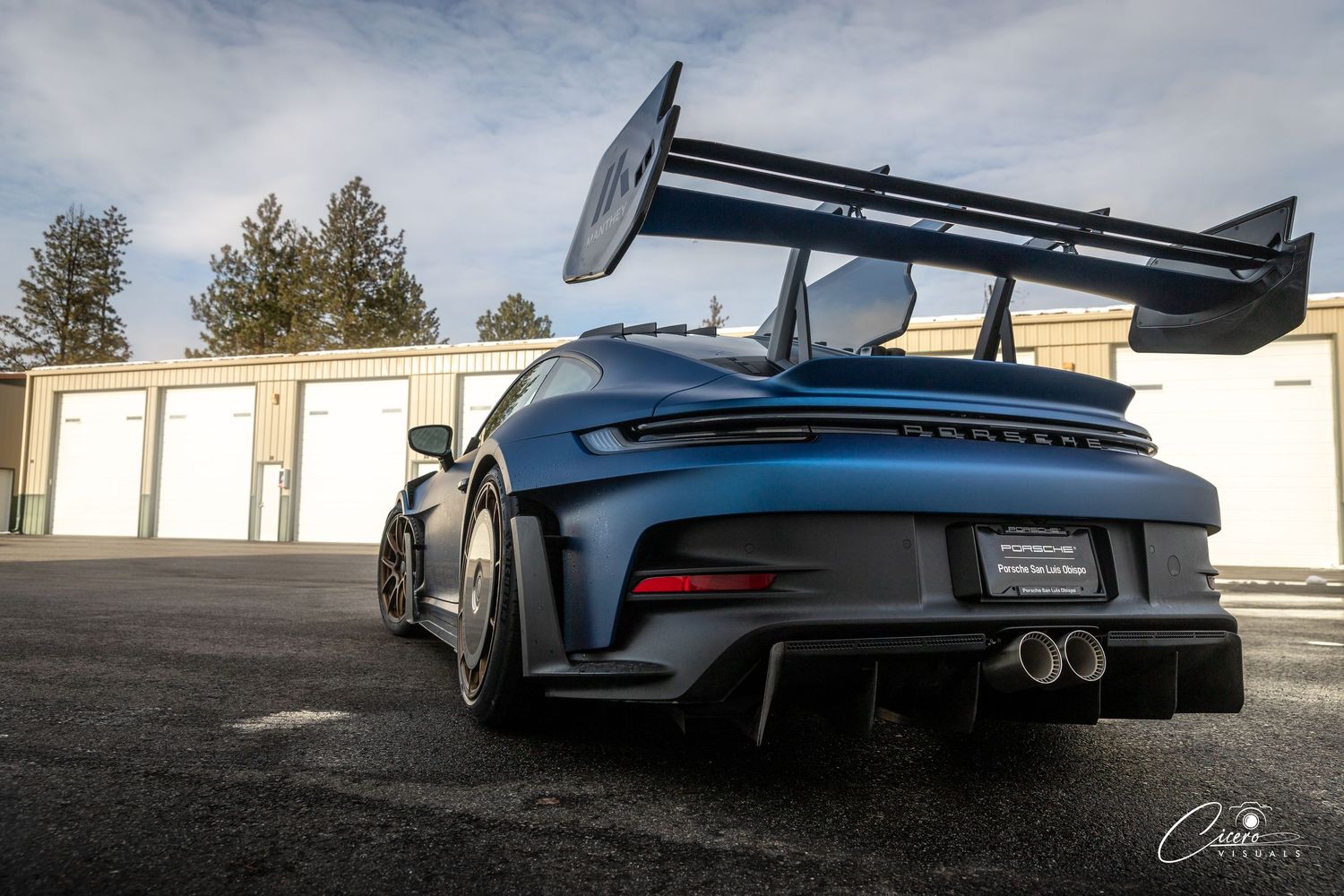 A sleek blue Porsche 911 GT3 sports car shown from multiple angles against a cloudy sky and storage facility background.